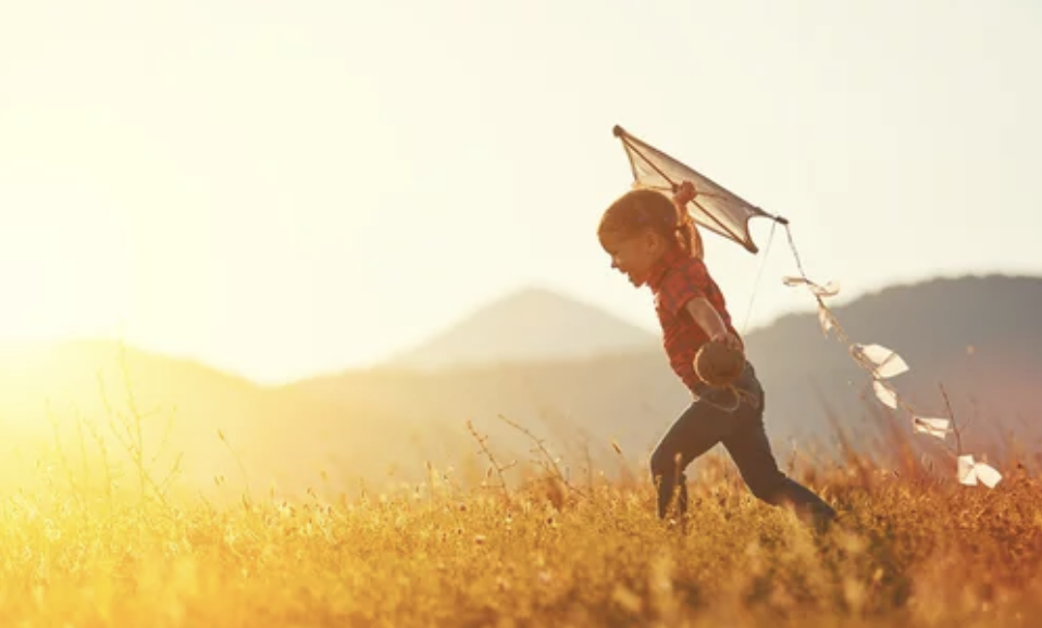 A young girl playing with a kite in a grassy field during sunset.
