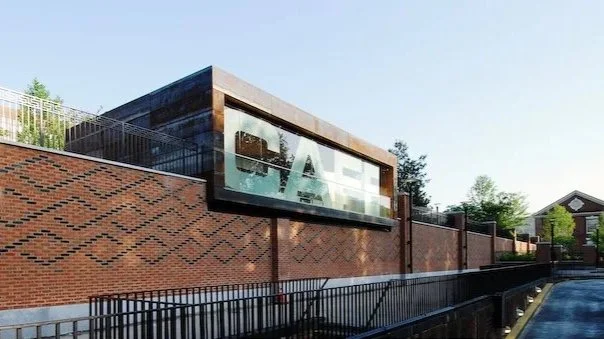 Exterior of a brick building with a large glass window that displays the word "CAFE". brahlerdesign.