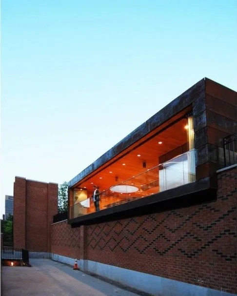 Modern building with a brick lower level and an illuminated glass upper deck with a person standing inside. brahlerdesign.
