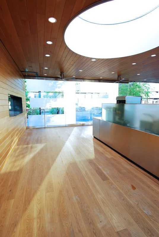 Modern lobby with wooden walls and floors, with a curved ceiling feature and large glass windows letting in natural light. brahlerdesign.