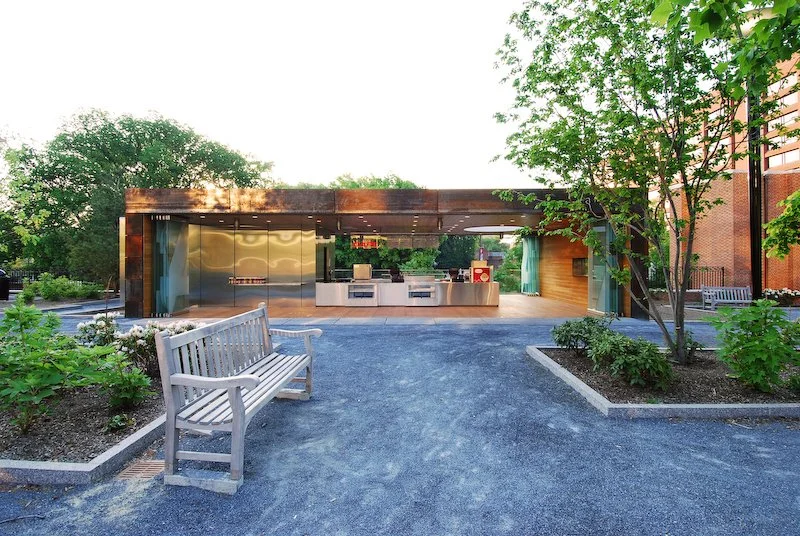 Outdoor food court with modern kitchen, surrounded by trees and benches. brahlerdesign.