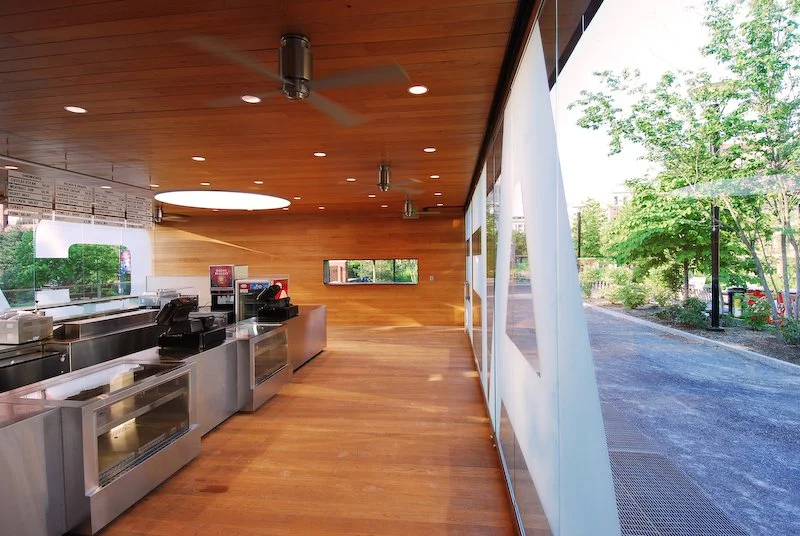 Empty fast-food restaurant or cafeteria with large window, wooden interior, and stainless steel service counters. brahlerdesign.