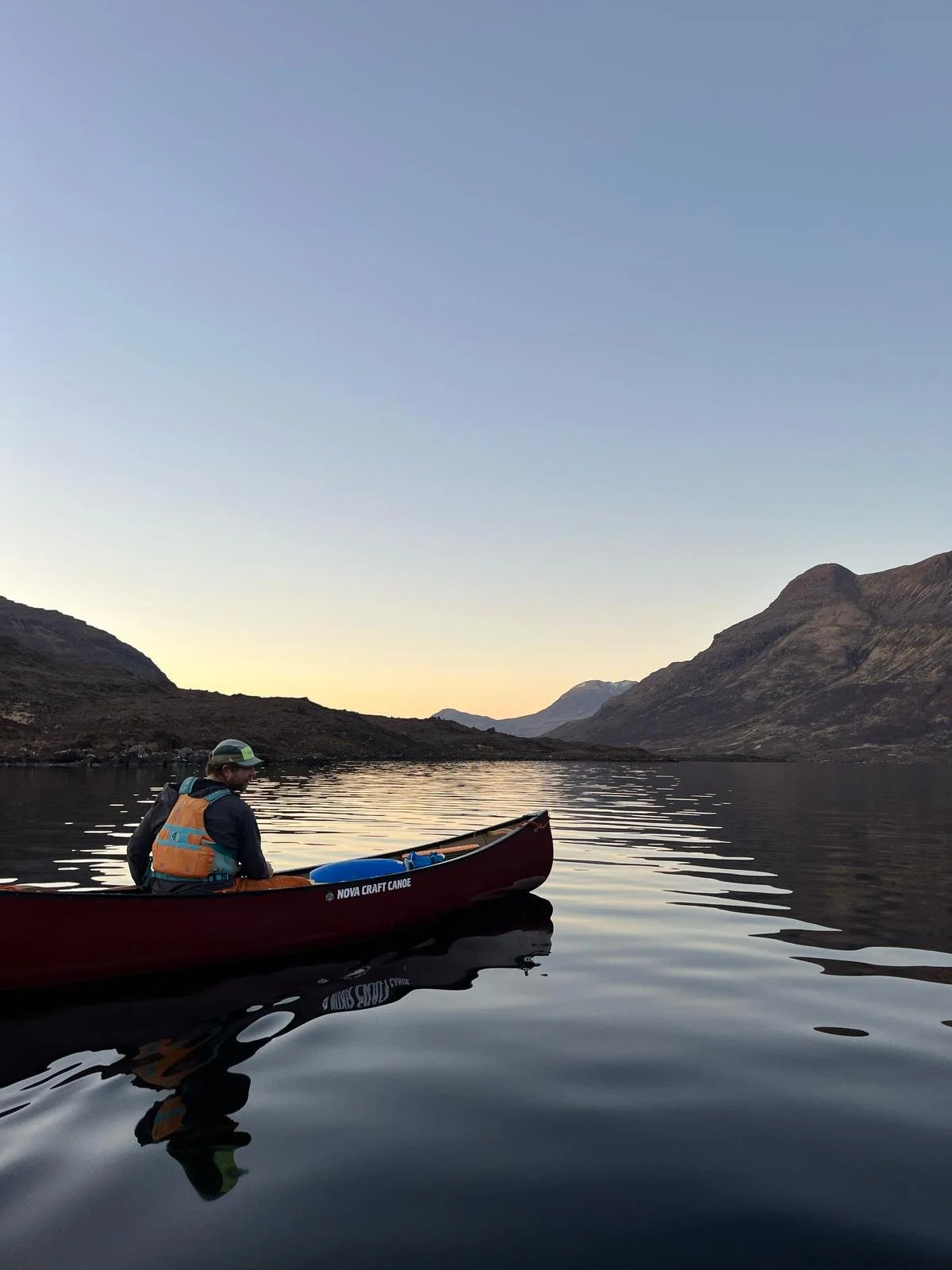 Person kayaking on a calm lake with mountain landscape during sunset or sunrise.