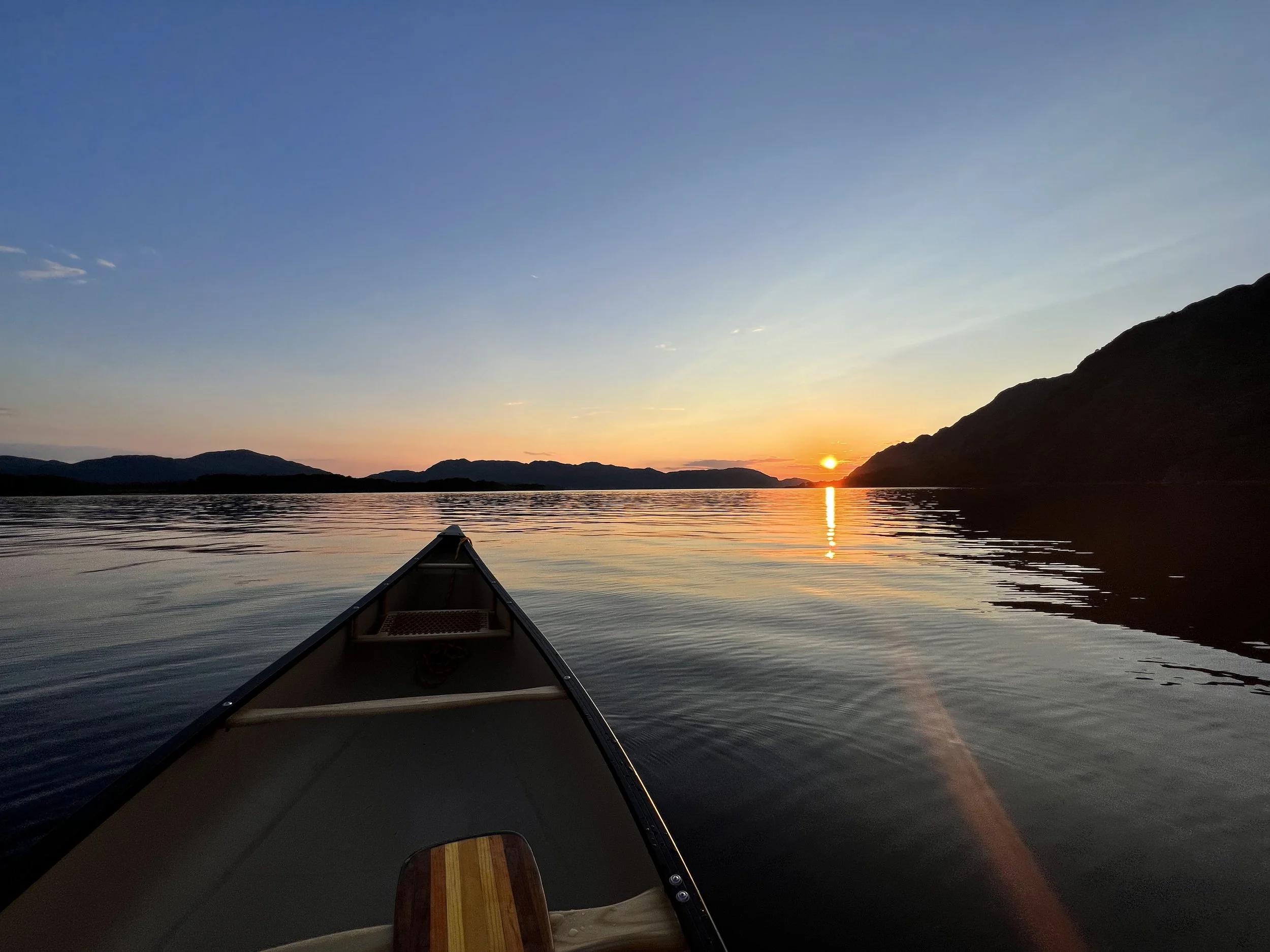 View from a canoe on a calm lake at sunset with mountains in the distance.
