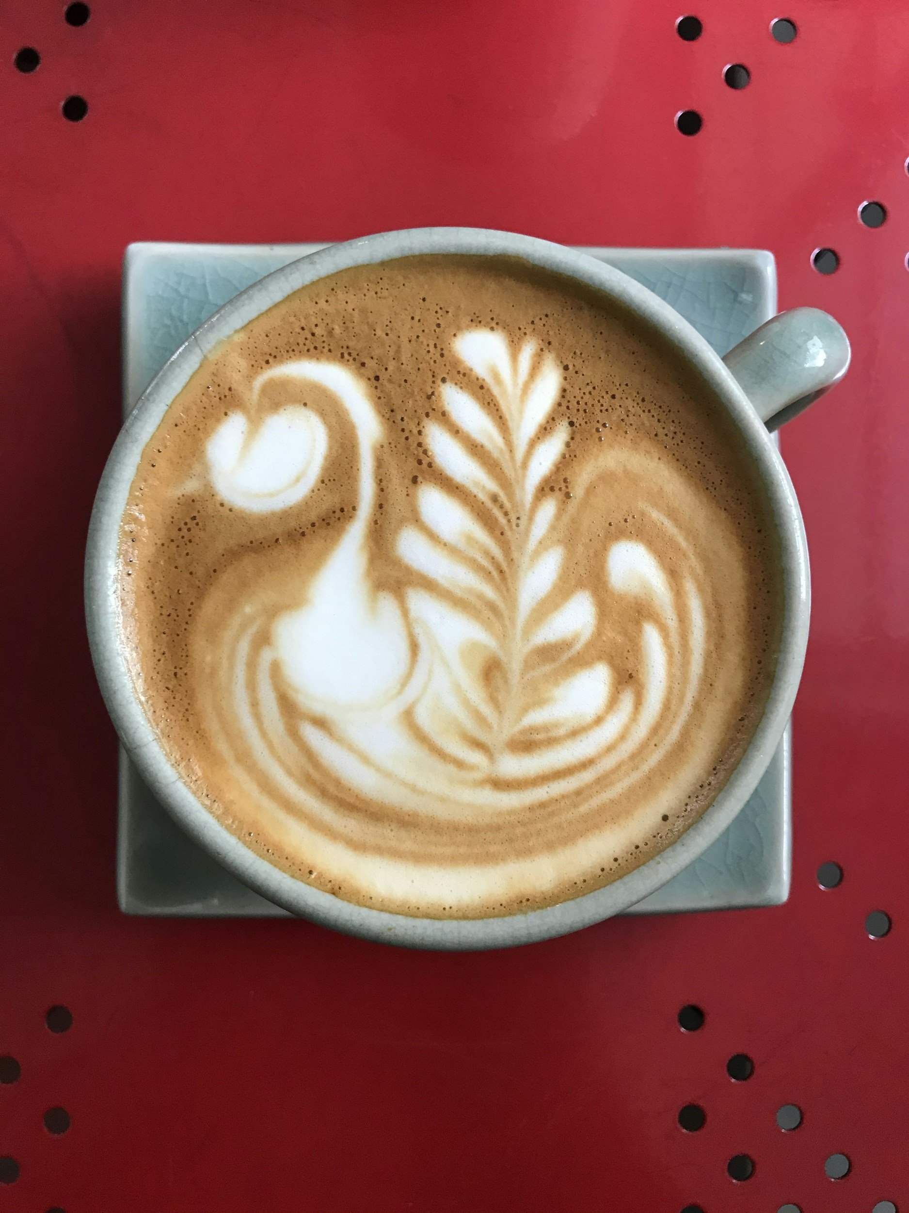 A latte with latte art of a swan and a leafy pattern on top, served in a light blue ceramic cup on a matching saucer.