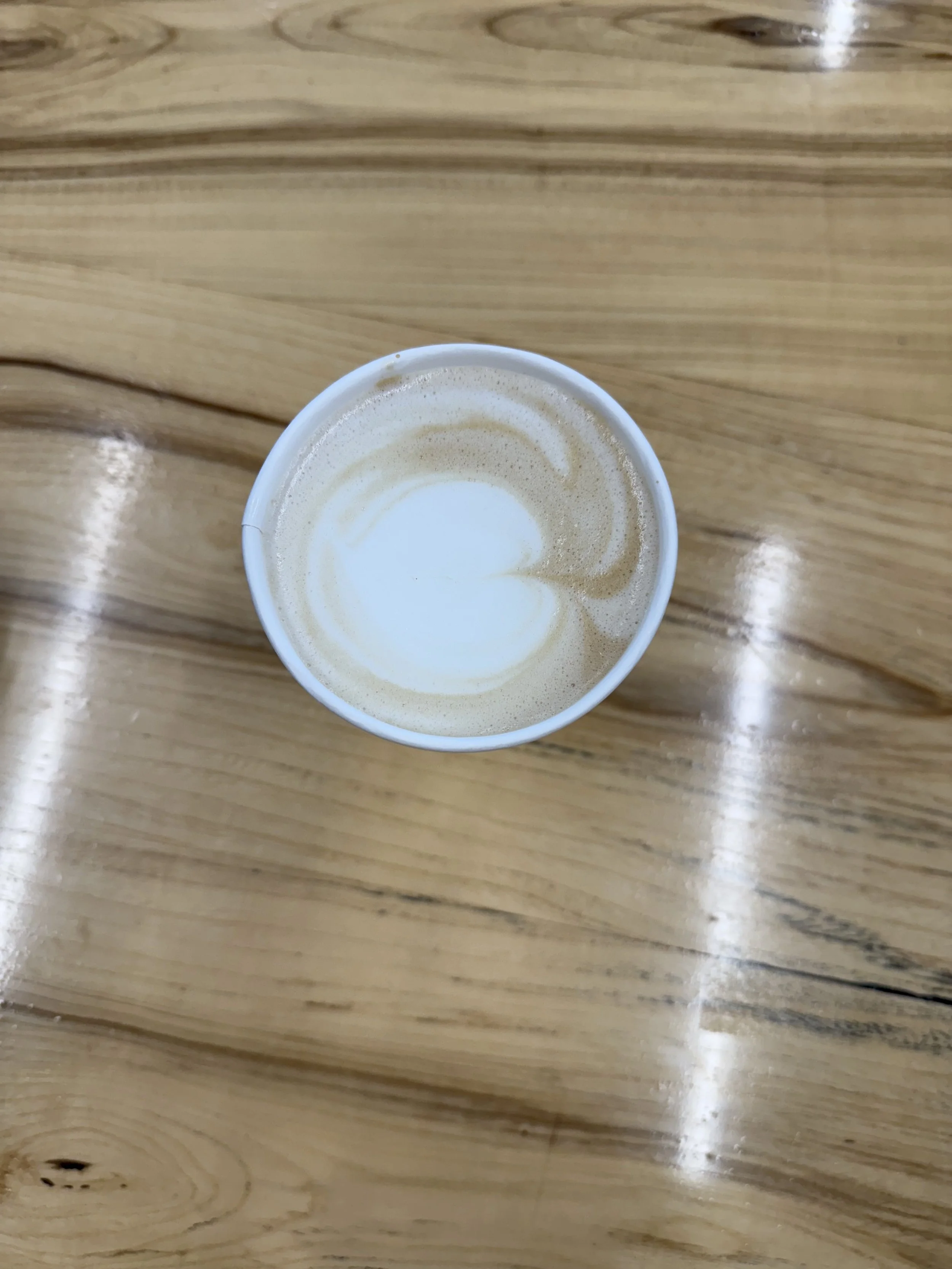 A top-down view of a coffee cup with latte art on a wooden table.