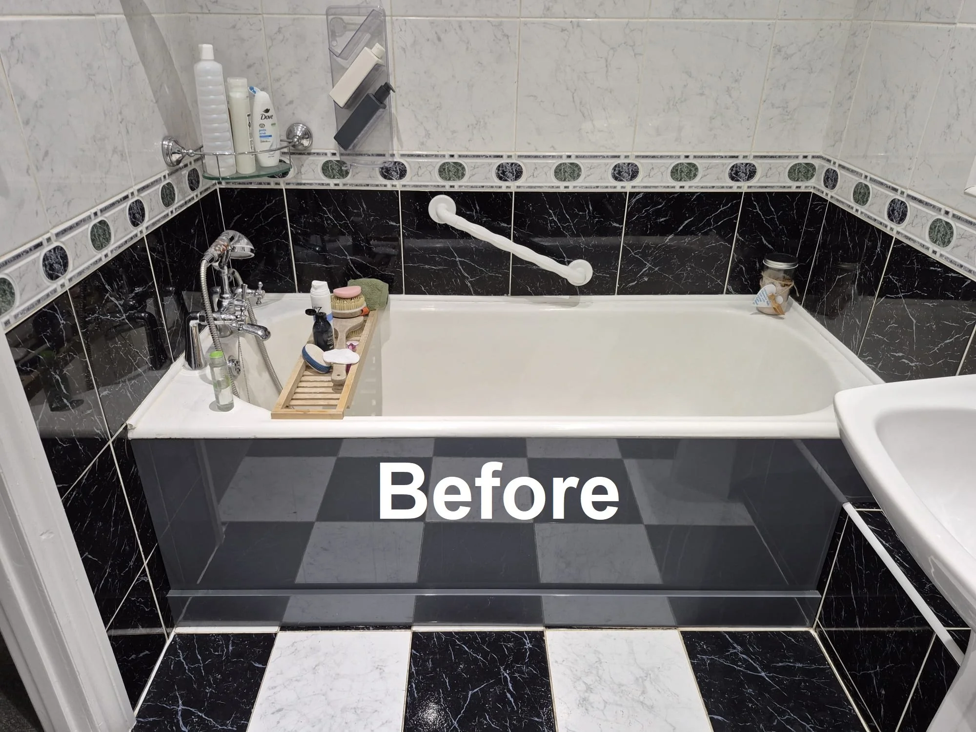 A bathroom with a black and white tiled floor and walls, featuring a bathtub filled with water, a grab bar, and toiletries on a tray and shelf.