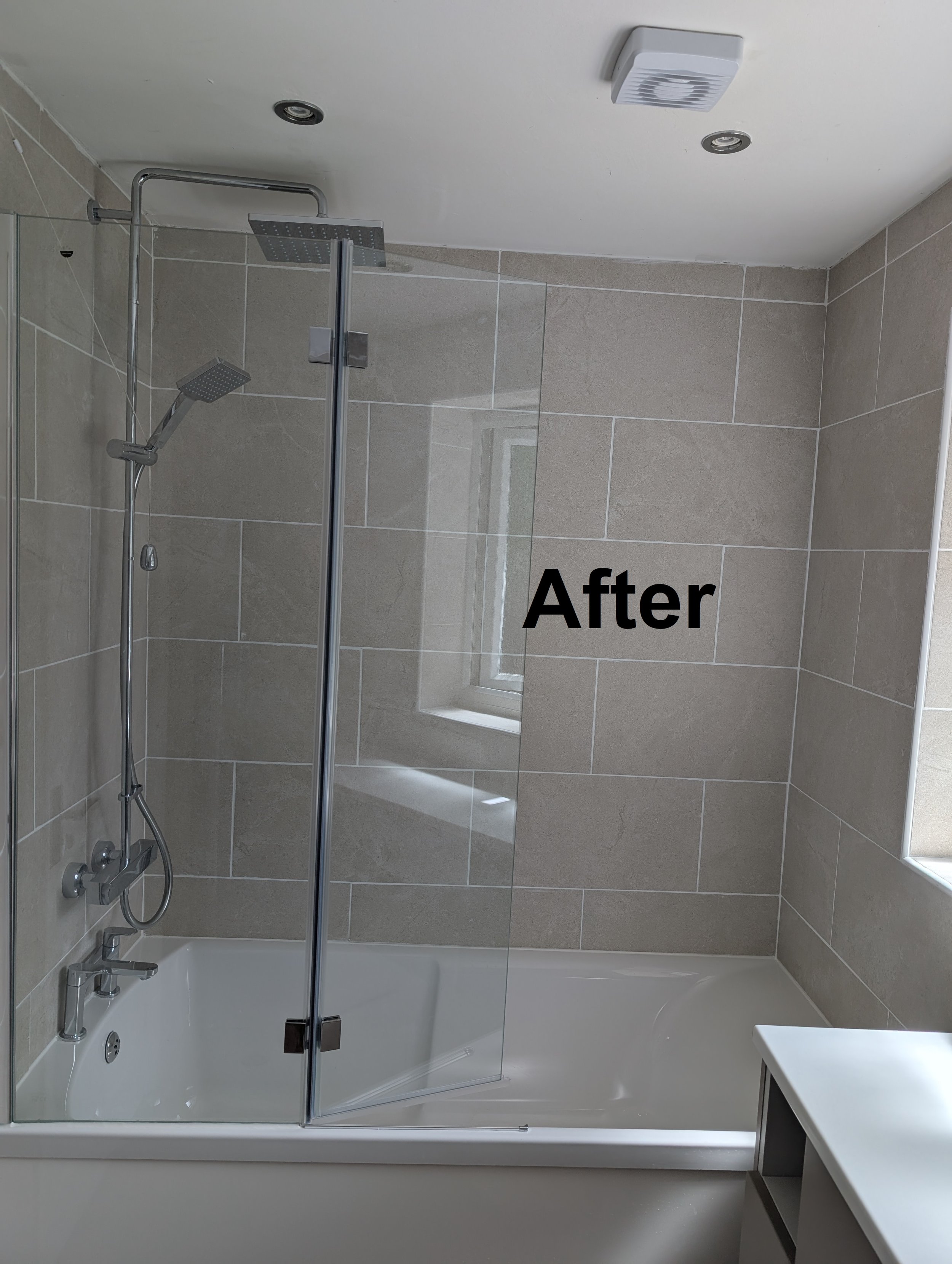 A modern bathroom shower with beige tiled walls, a glass shower enclosure, a rainfall showerhead, a handheld showerhead, a small window, a white bathtub, and a part of a white vanity. The word "After" is written in black on the image.