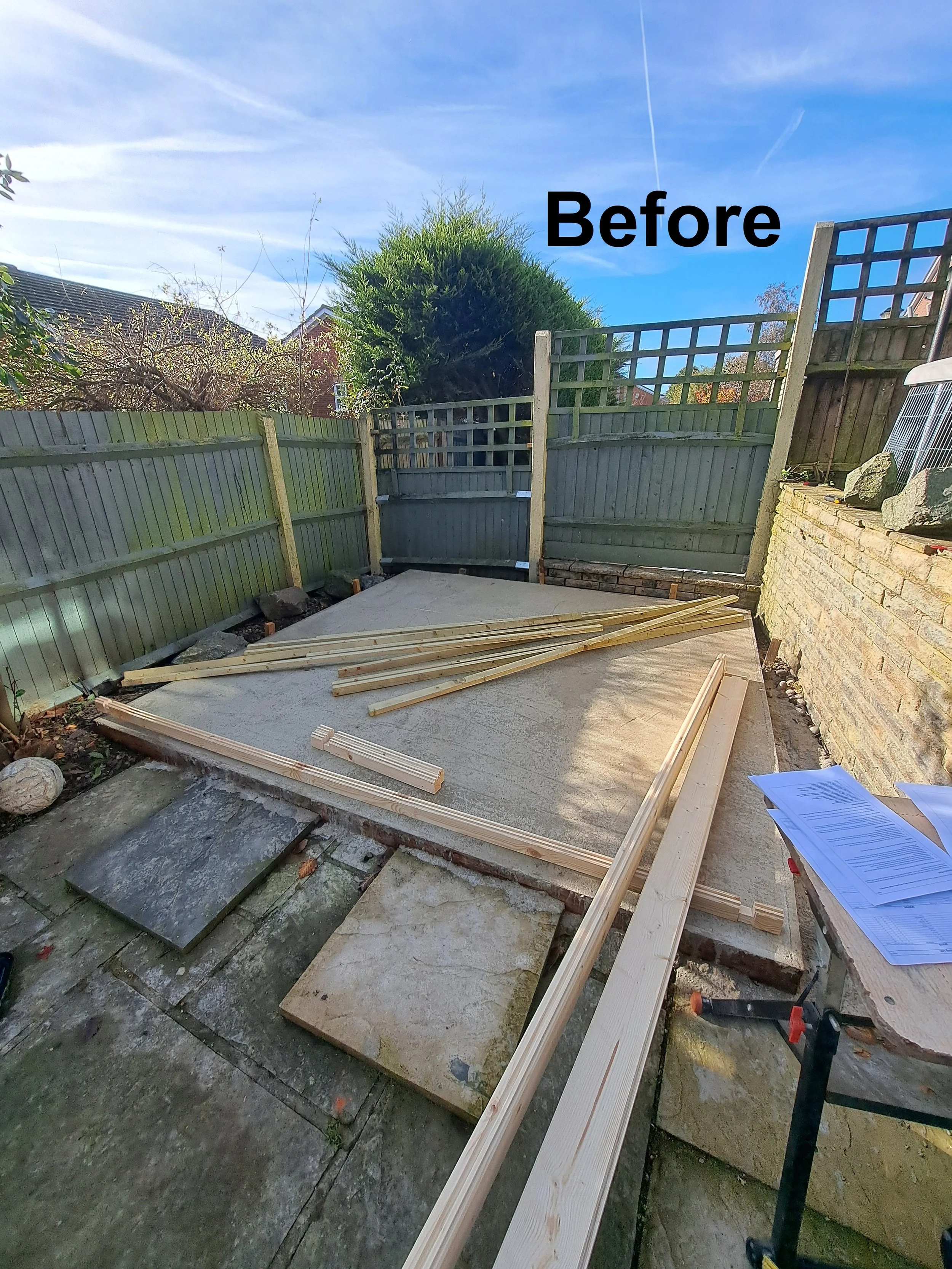Backyard with a new wooden fence being installed, some wooden planks on the ground, papers on a nearby table, and a label 'Before' on the image.