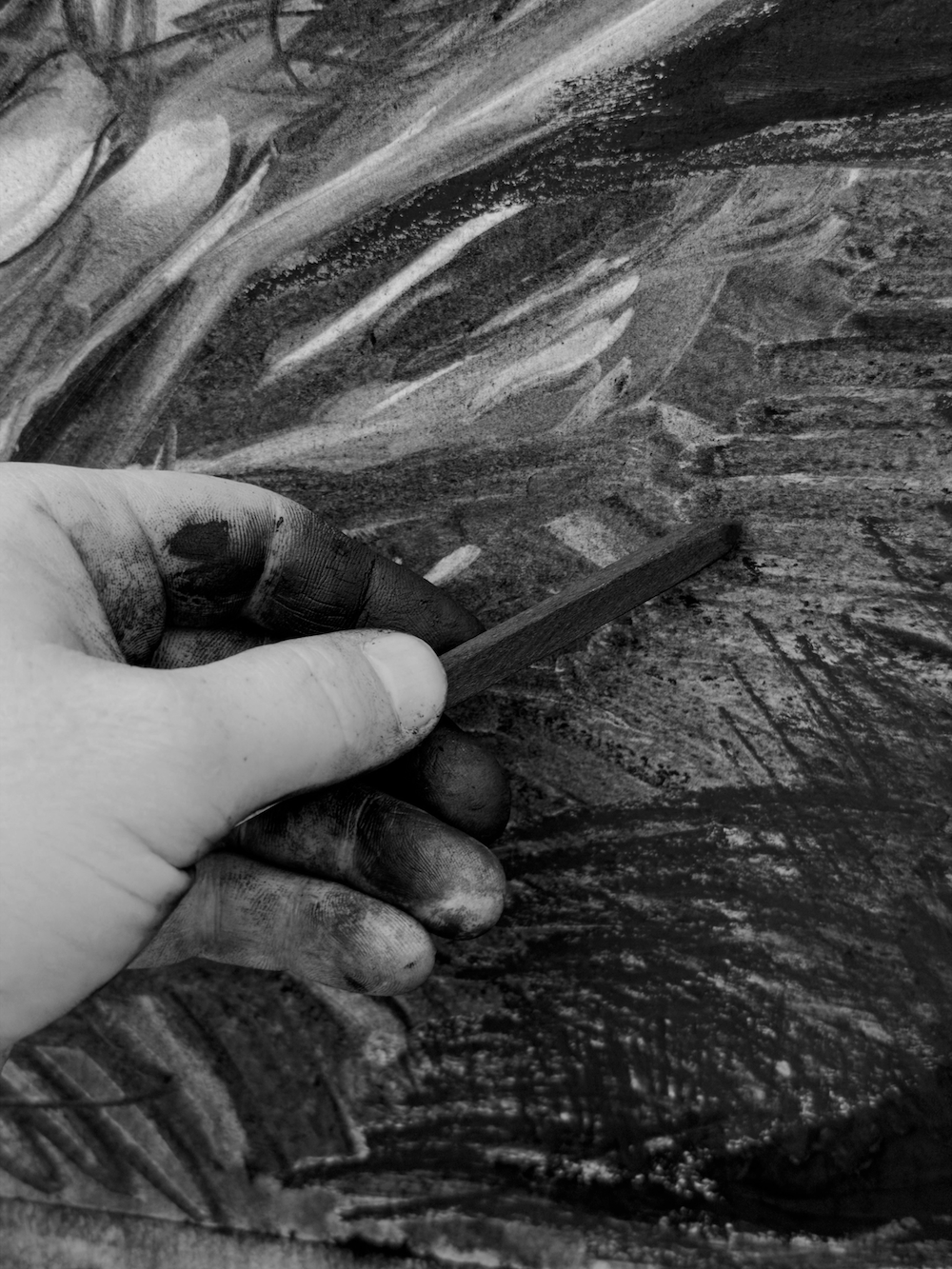 Close-up of a hand holding a piece of charcoal, drawing abstract patterns on a textured surface.