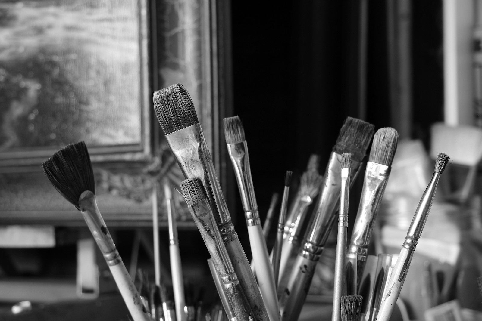 A collection of paintbrushes with varying sizes and shapes, placed in a container near a window in an art studio.