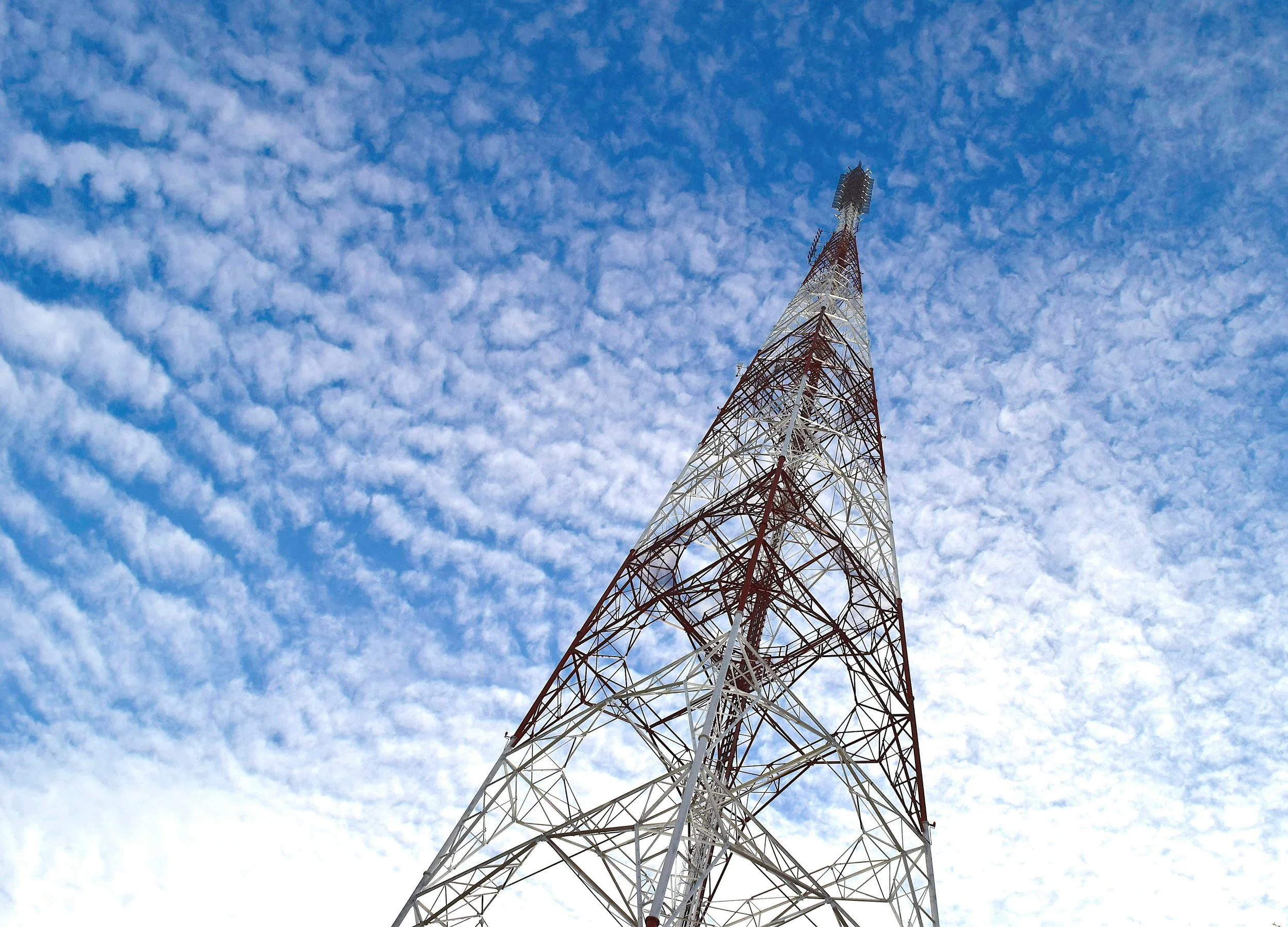 A tall radio tower painted red and white, extending into a blue sky filled with scattered small clouds.