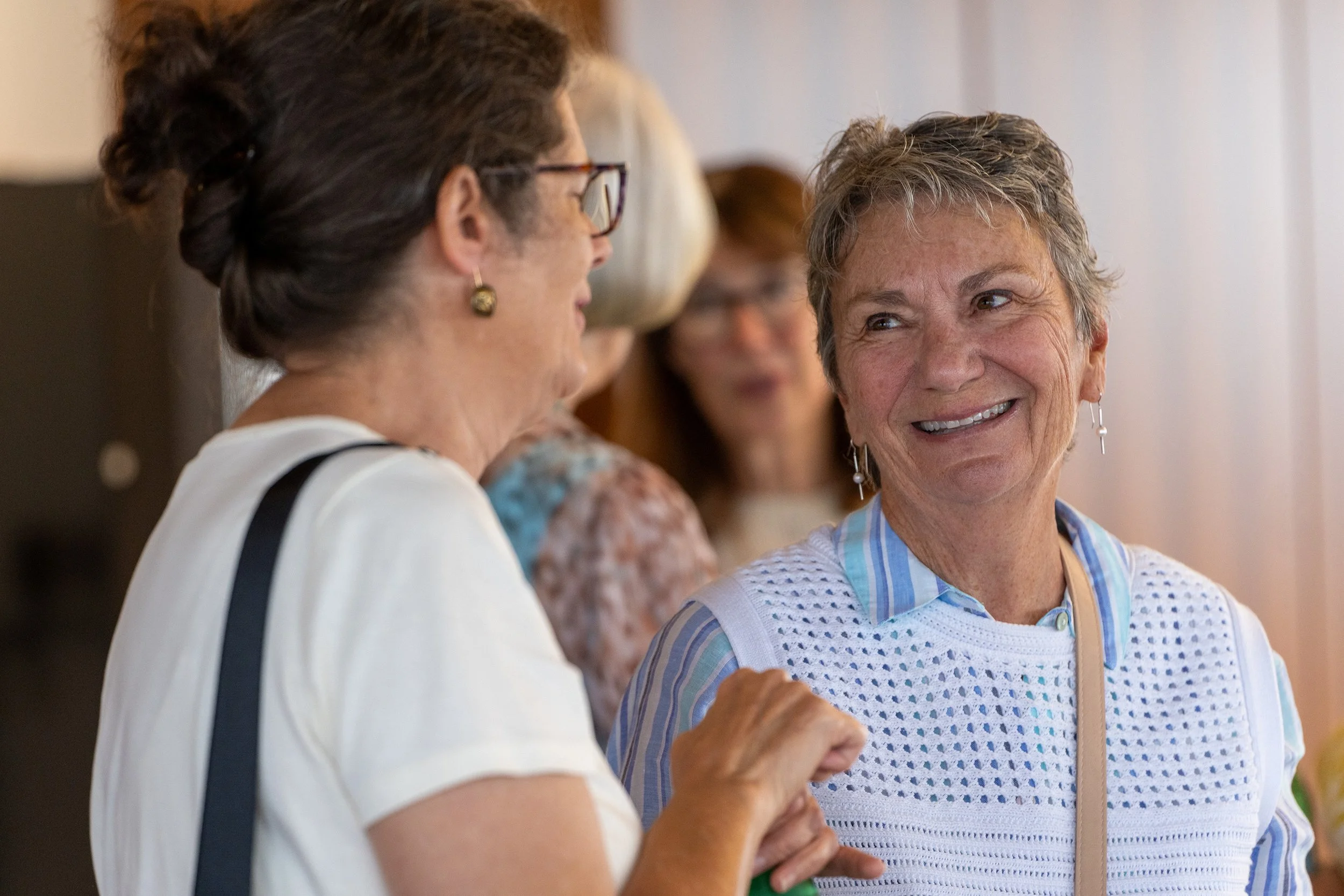 Two women engaged in a conversation at a social gathering, with the woman on the right smiling warmly.