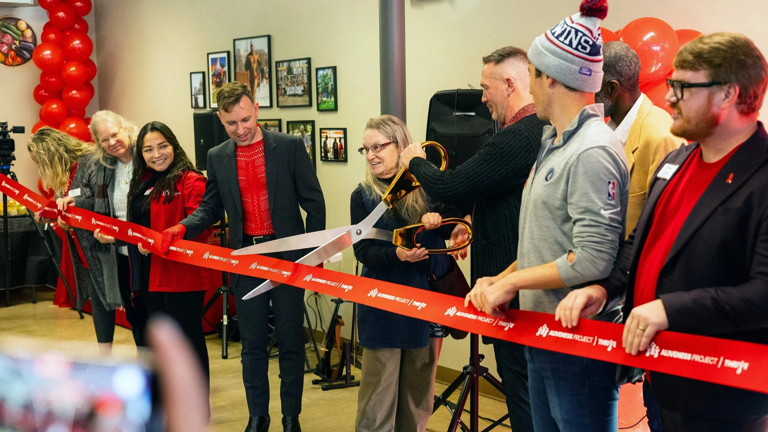 People at a ribbon-cutting ceremony, holding a large pair of scissors to cut the red ribbon marked 'Auntie Anne's'.