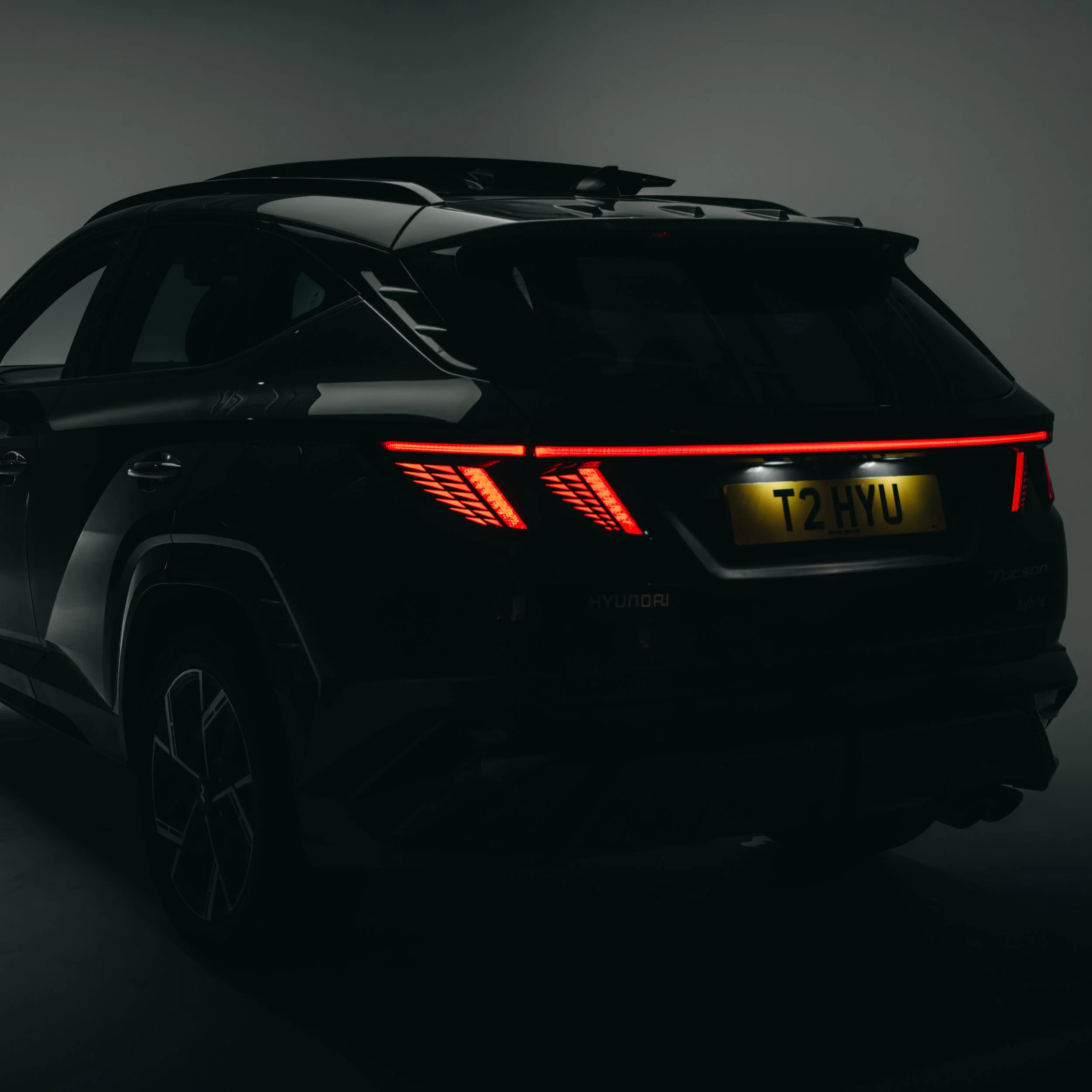 A black Hyundai Tucson hybrid SUV with illuminated red tail lights, parked in a dimly lit environment.