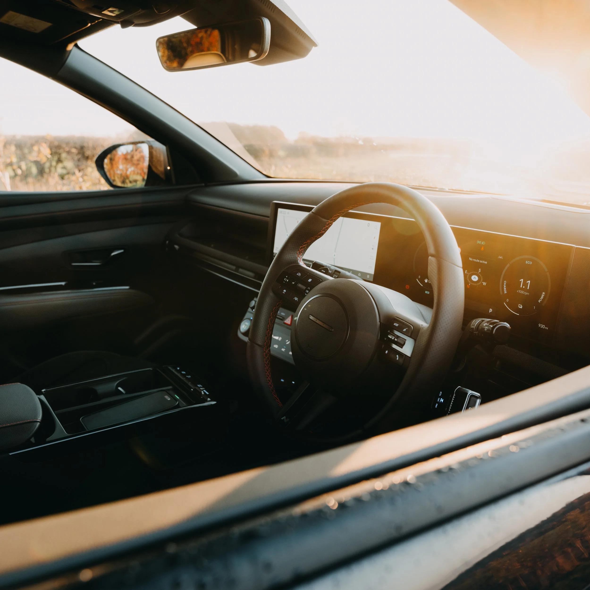Inside view of a modern car with a digital dashboard and steering wheel, sunlight shining through the windshield.