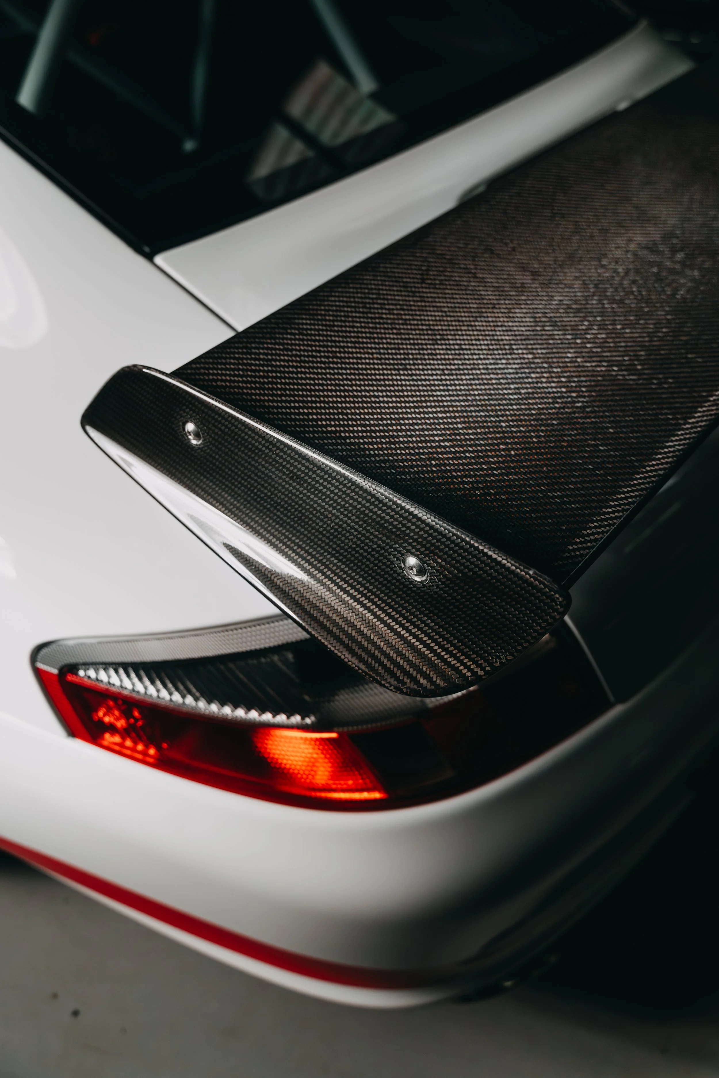 Close-up of the rear of a car with a carbon fiber rear wing and taillight, showing a sleek, high-performance design.