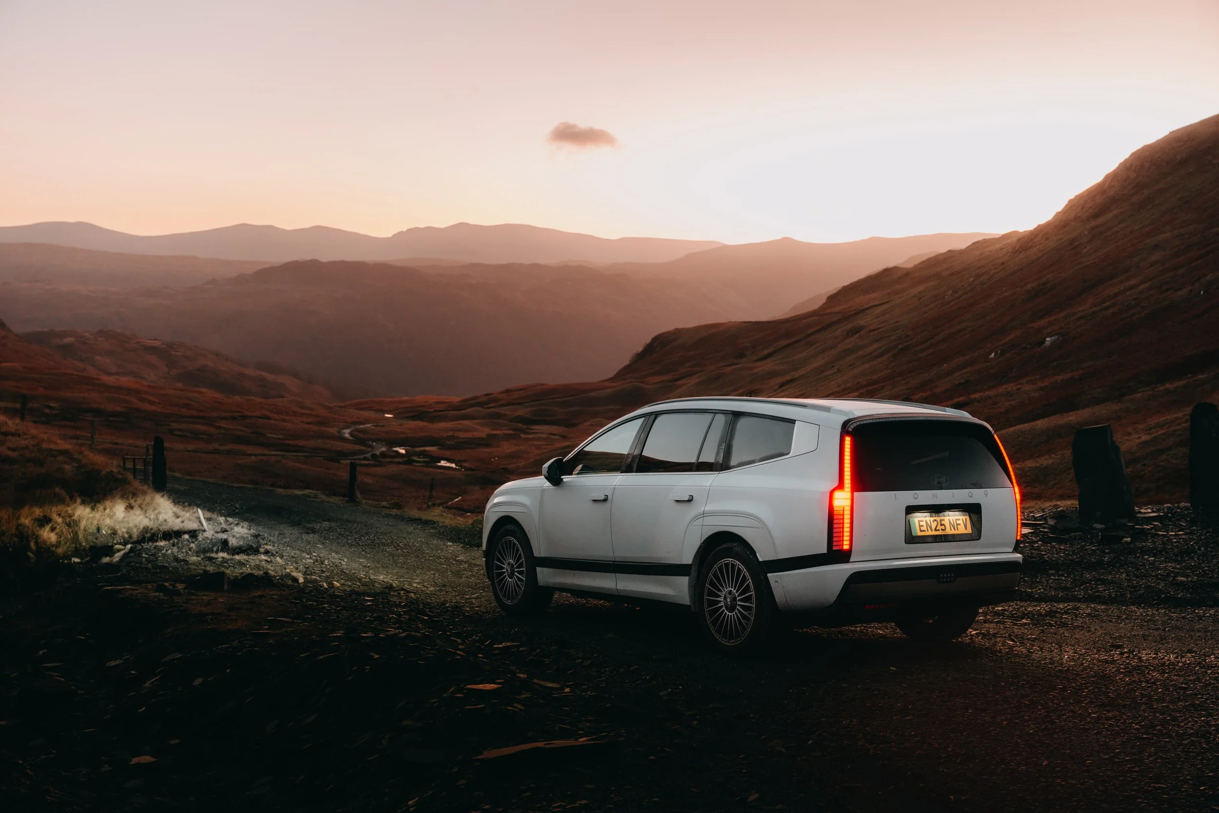 A white motorhome parked on a dirt road in a landscape with rolling hills and mountains at sunset.