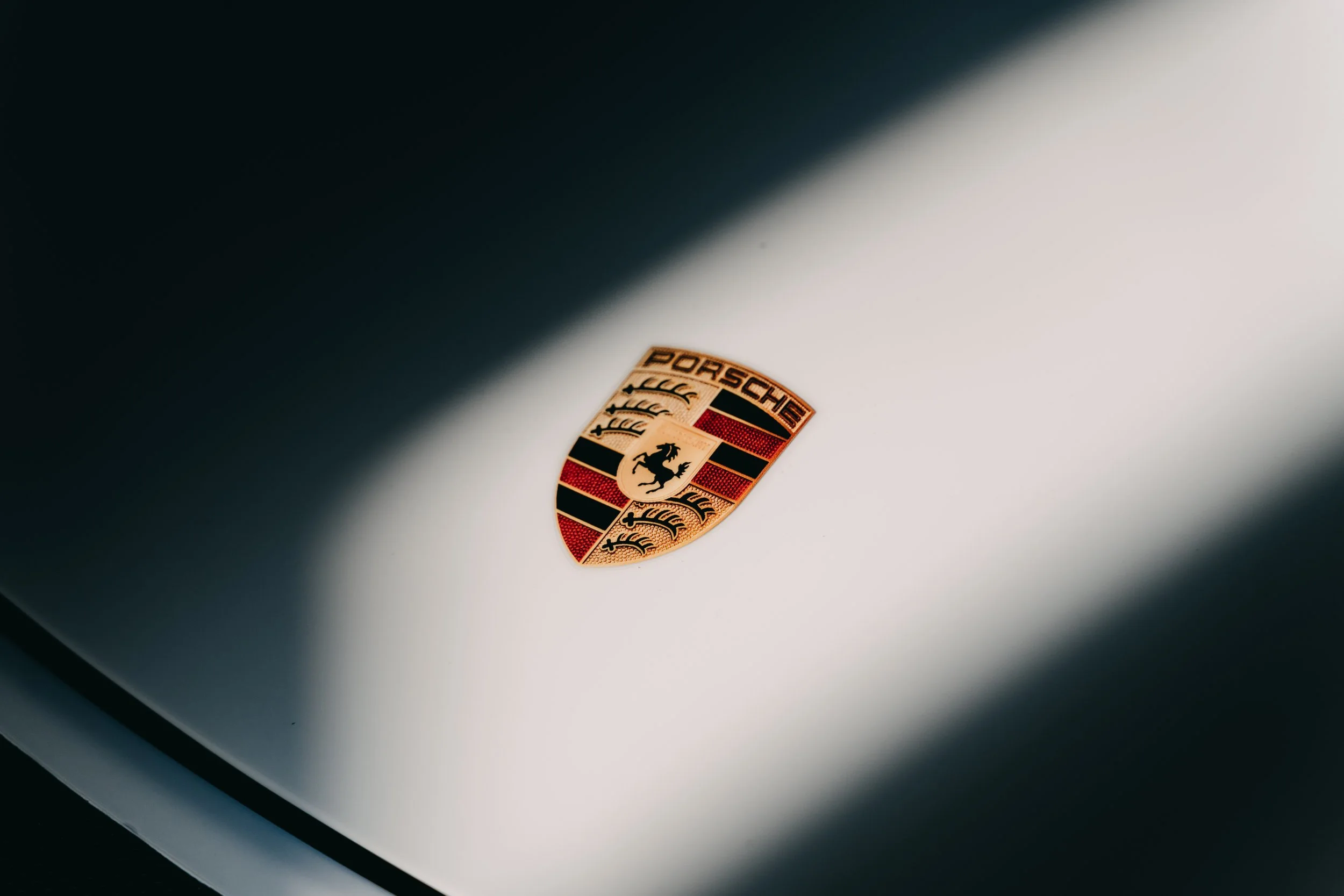 Close-up of a Porsche logo on the hood of a vehicle with a gradient shadow.