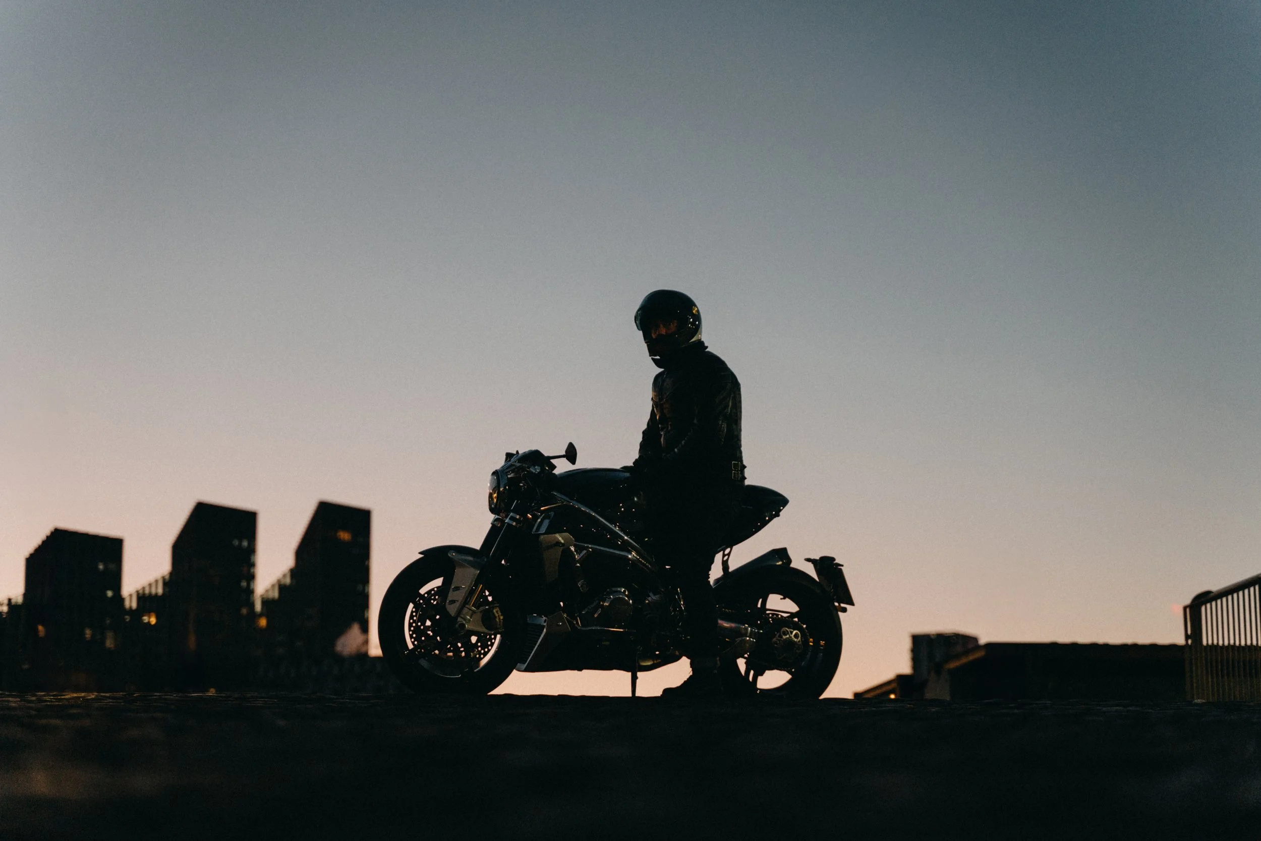 Silhouette of a person wearing a helmet sitting on a motorcycle during sunset or dawn
