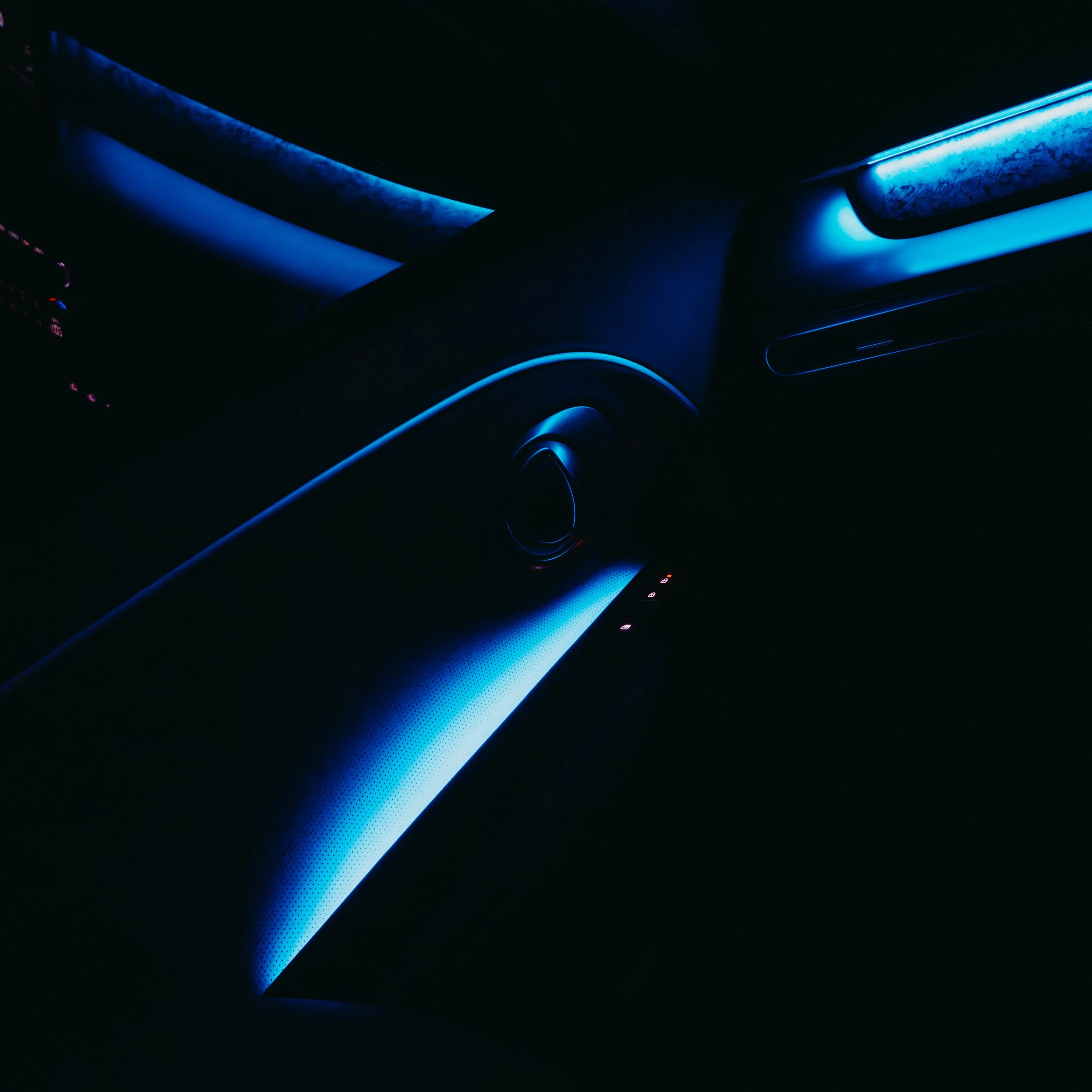 Close-up of the interior of a car with blue ambient lighting, showing part of the dashboard and air vent in a dark setting.