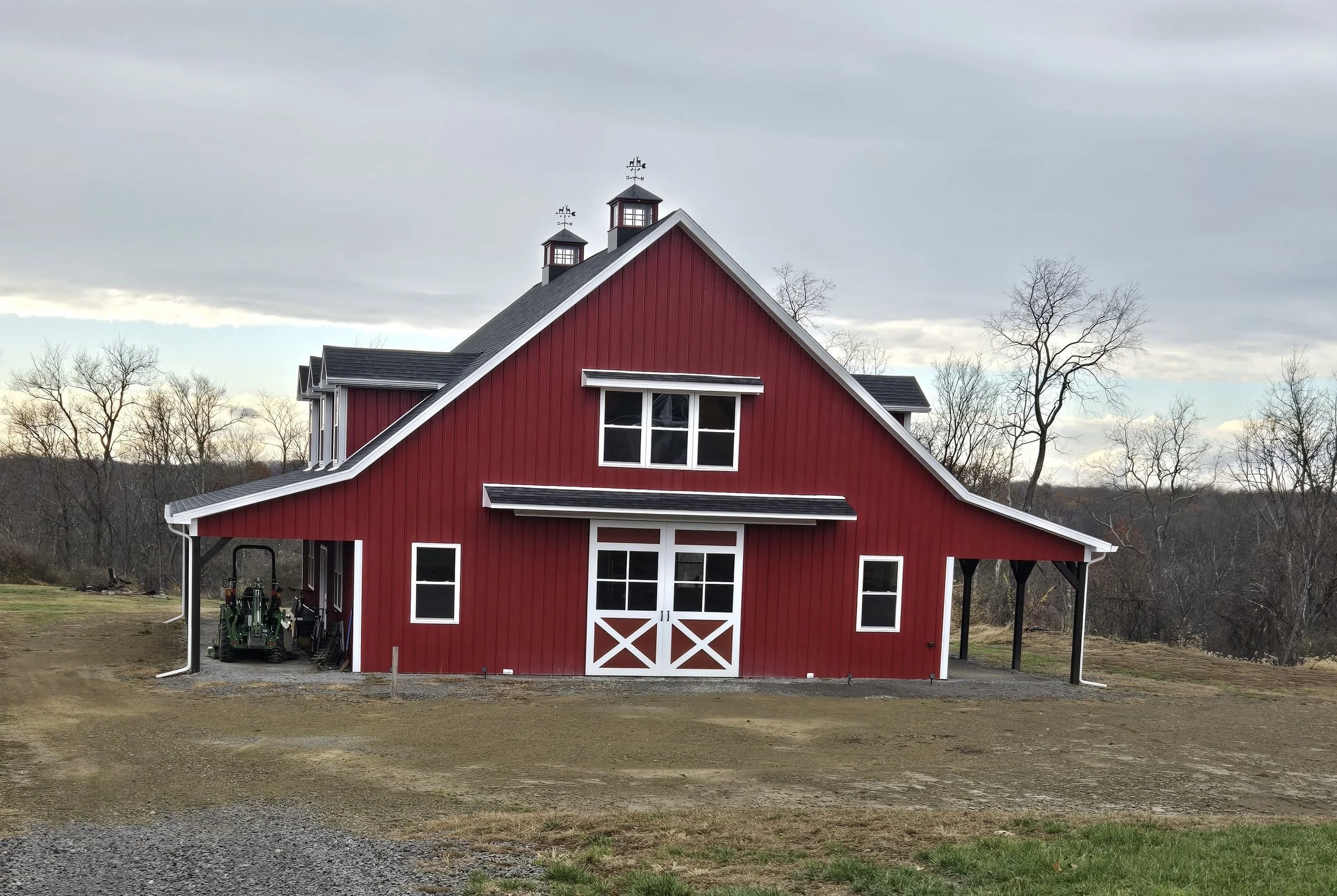 Red barn with white trim and black roof, set in rural landscape with trees and open sky.