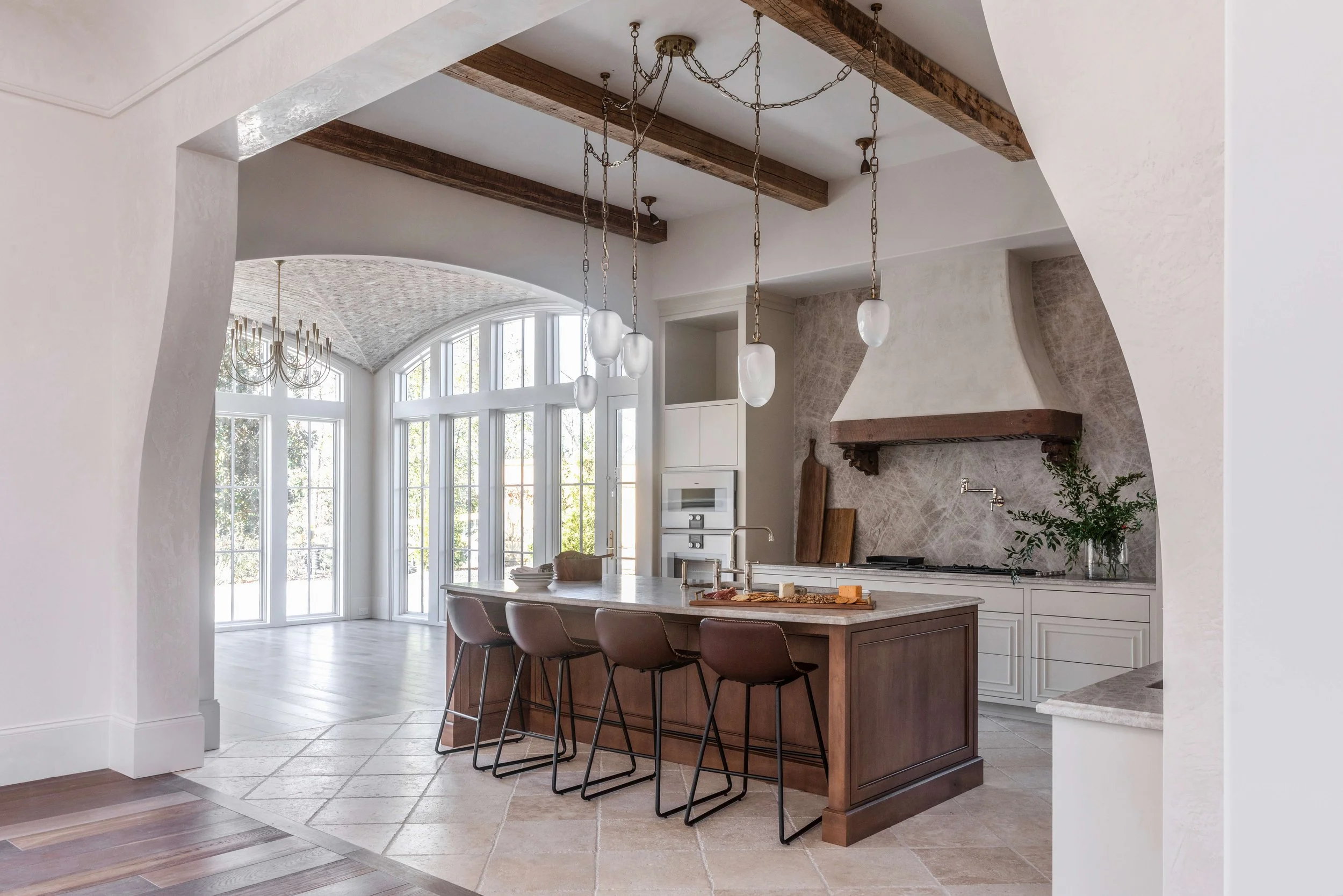 View through a black-framed glass door opening inside to a spacious room with light-colored walls, large windows, and hardwood floors. Two wall-mounted wooden lanterns are on either side of the door, and a small elevation change is visible inside the room.