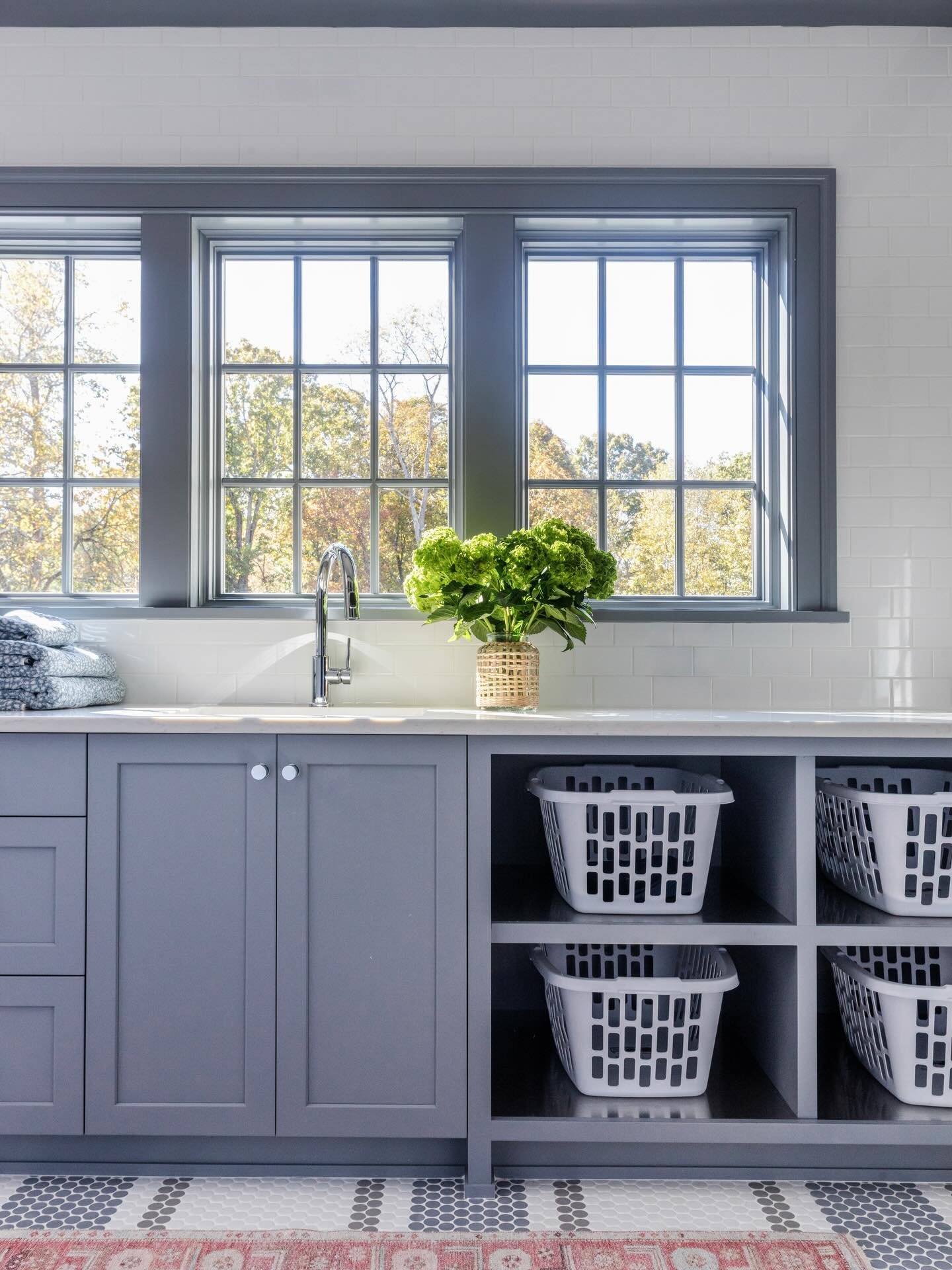 When a secondary space is crafted with the same care as the rest of the home, even the everyday feels elevated. This light-filled laundry room pairs custom cabinetry with polished chrome fixtures, timeless penny tile, and thoughtfully integrated open