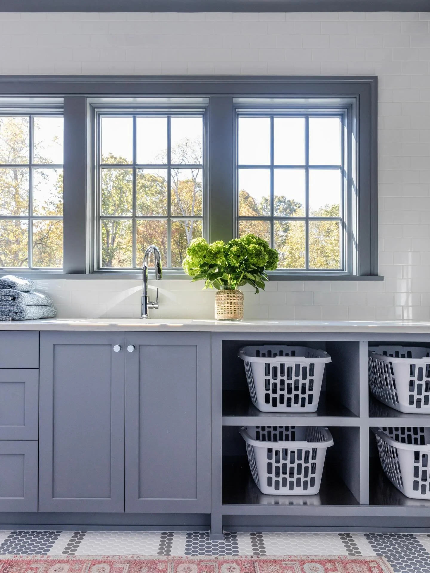 When a secondary space is crafted with the same care as the rest of the home, even the everyday feels elevated. This light-filled laundry room pairs custom cabinetry with polished chrome fixtures, timeless penny tile, and thoughtfully integrated open