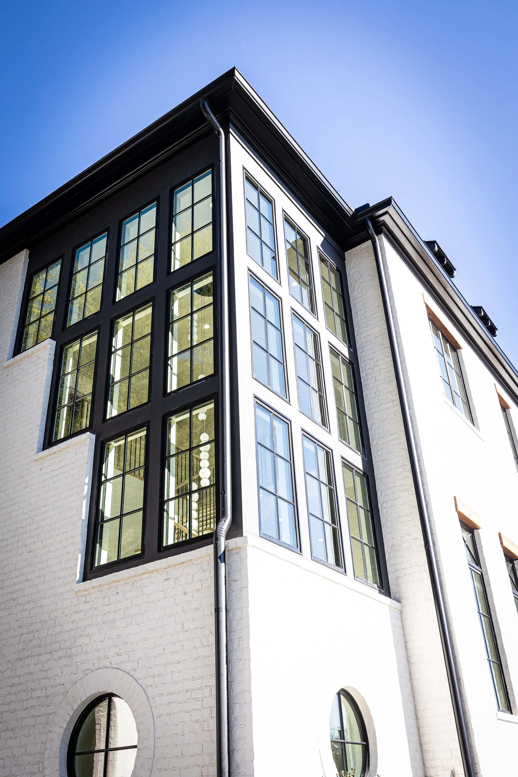 Modern multi-story custom home with large black-framed windows and white brick exterior, under a clear blue sky.