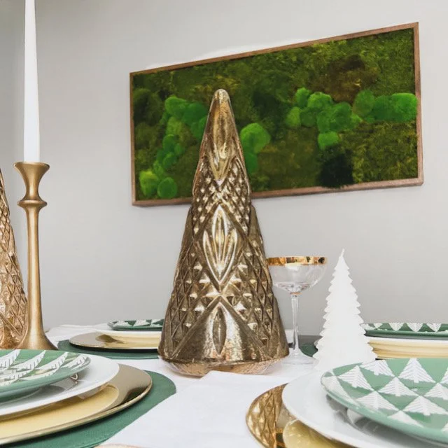 Decorative table setting with gold and green holiday-themed accents, including a gold cone centerpiece, white paper Christmas tree, and a green painting in the background.