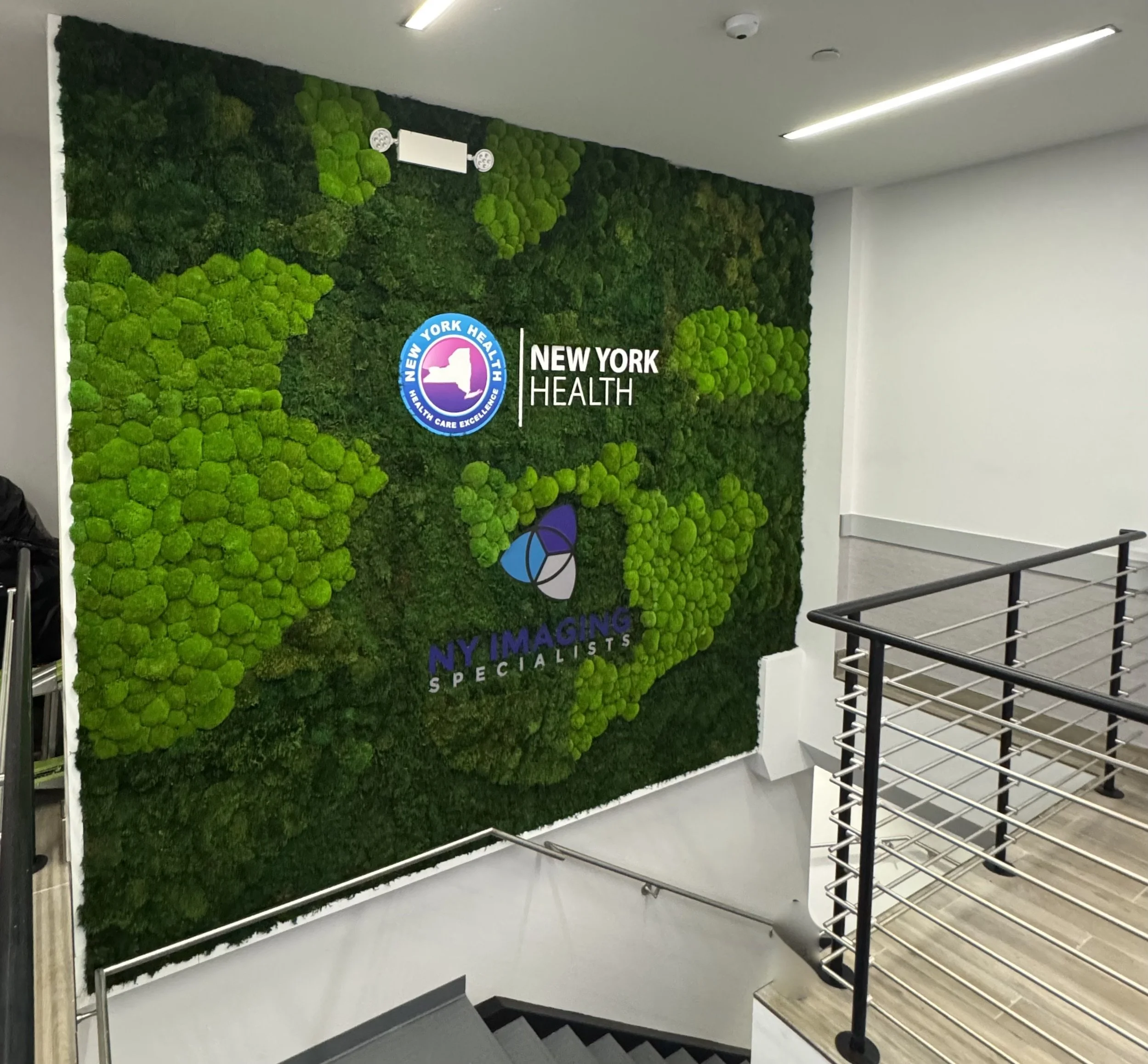 Green moss wall with logos of New York Health and Ny Imaging Specialists in an indoor office or clinic space.