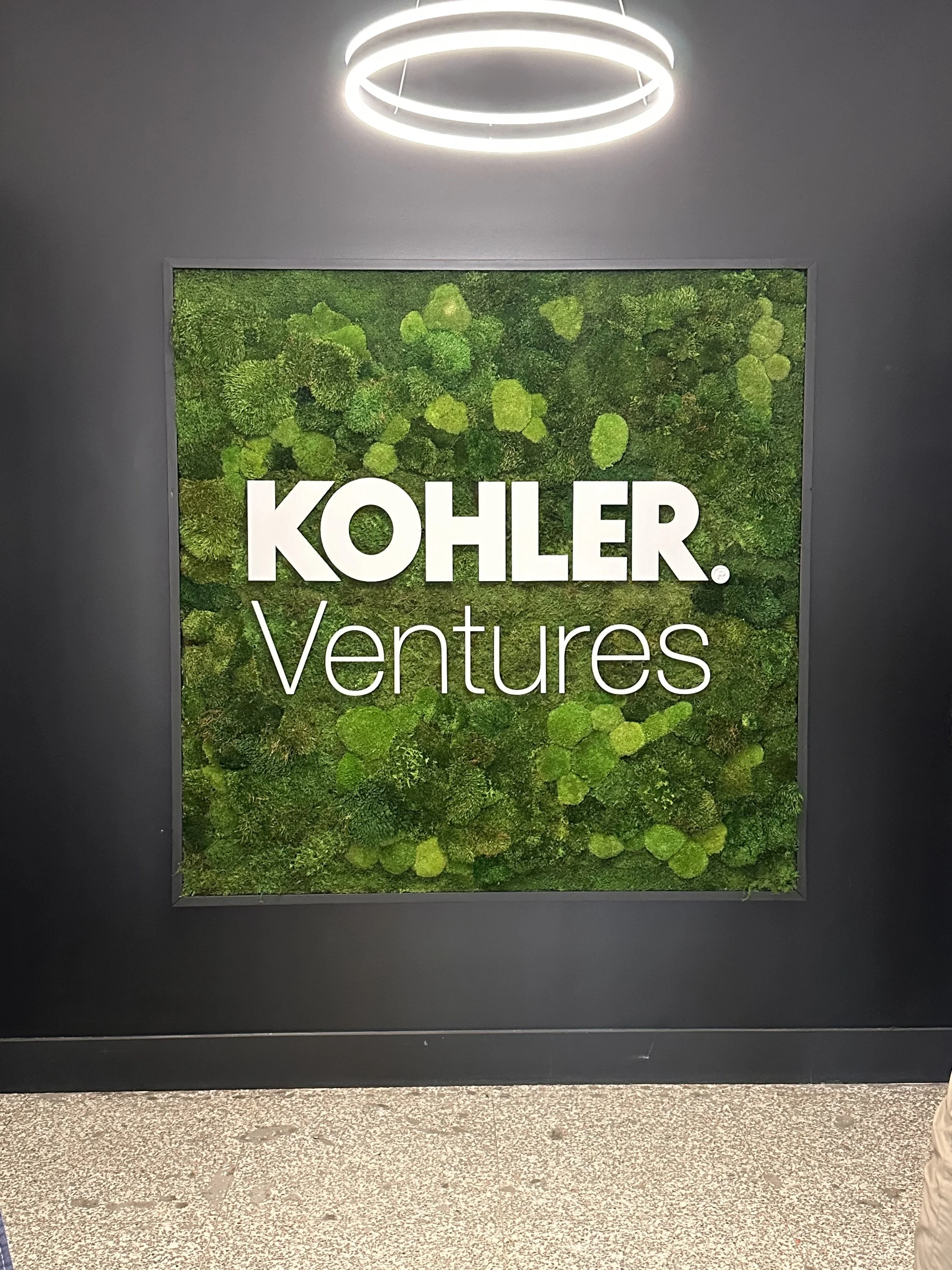 Kohler Ventures sign on a wall with green moss background.