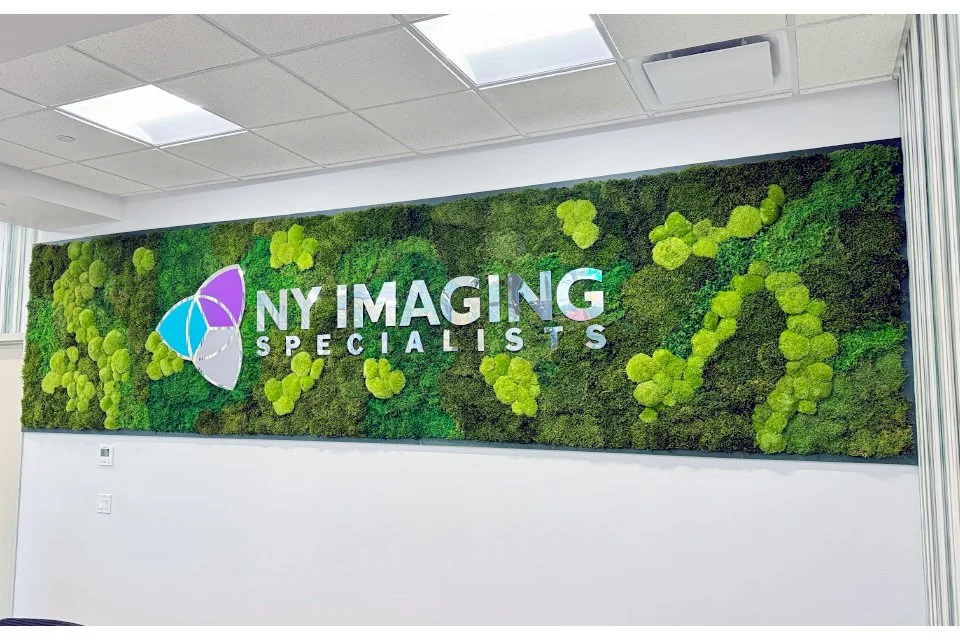 Interior office wall decorated with a green moss wall and the sign 'NY Imaging Specialists' with a colorful logo.