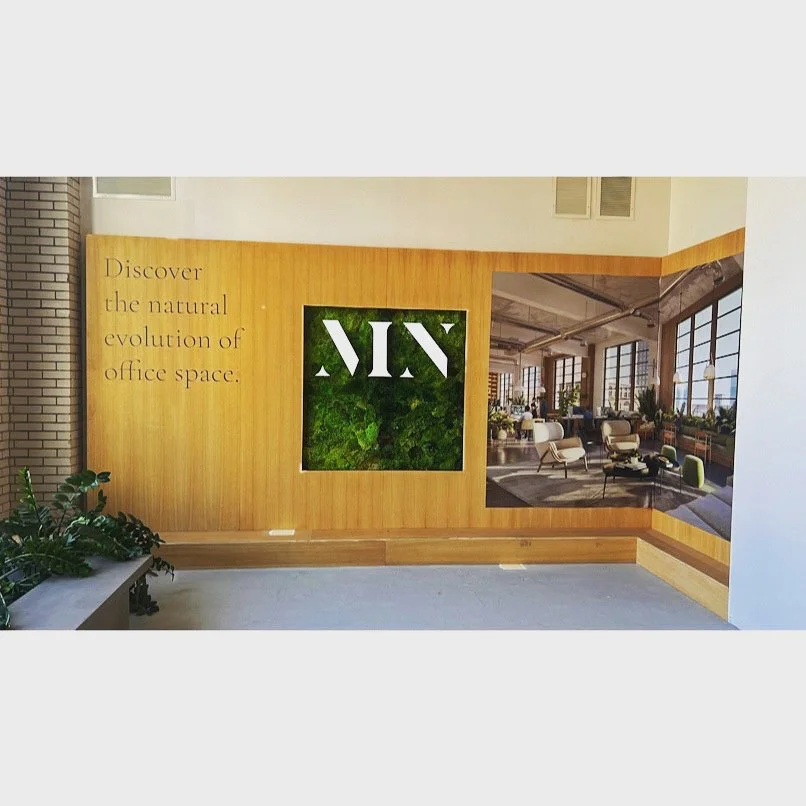 Wooden wall with text saying, "Discover the natural evolution of office space," a green logo with stylized letters, and a photograph of a modern, spacious office with large windows and contemporary furniture.