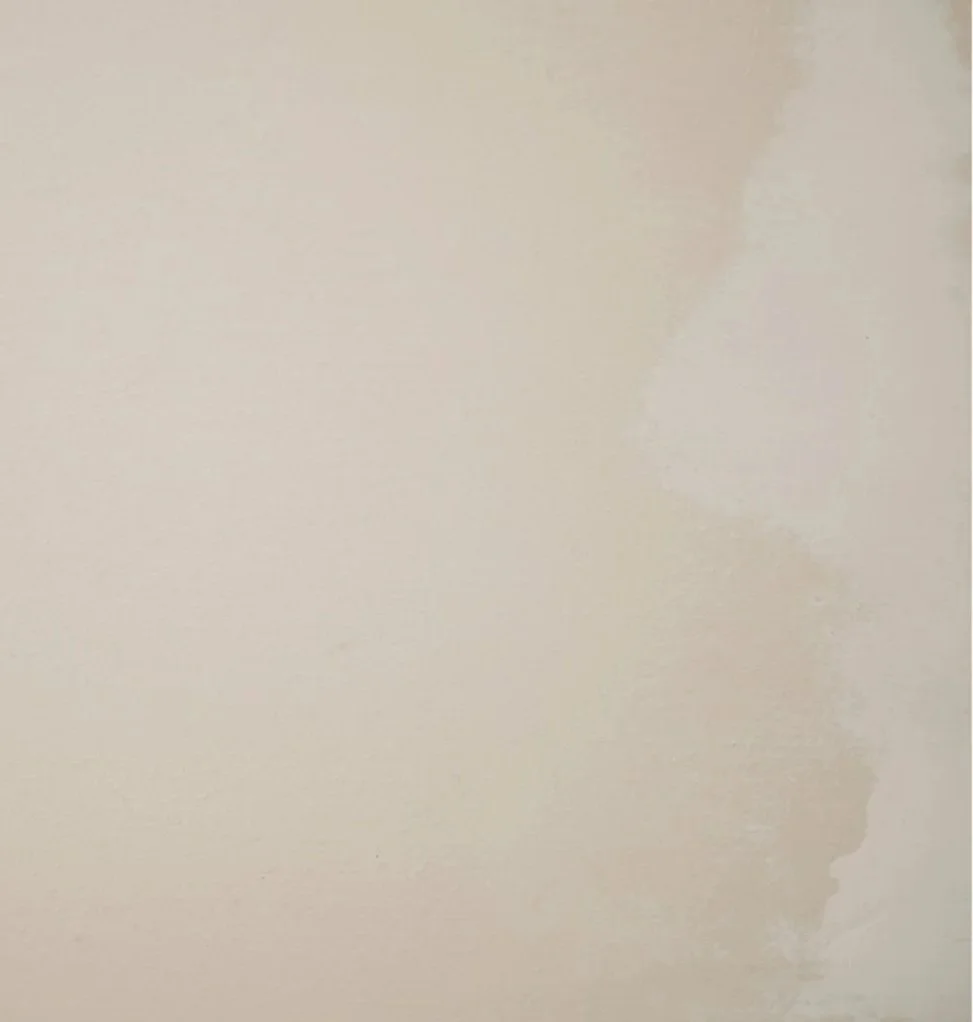 Close-up of a worn, slightly damaged painted wall or ceiling with a beige or off-white color.