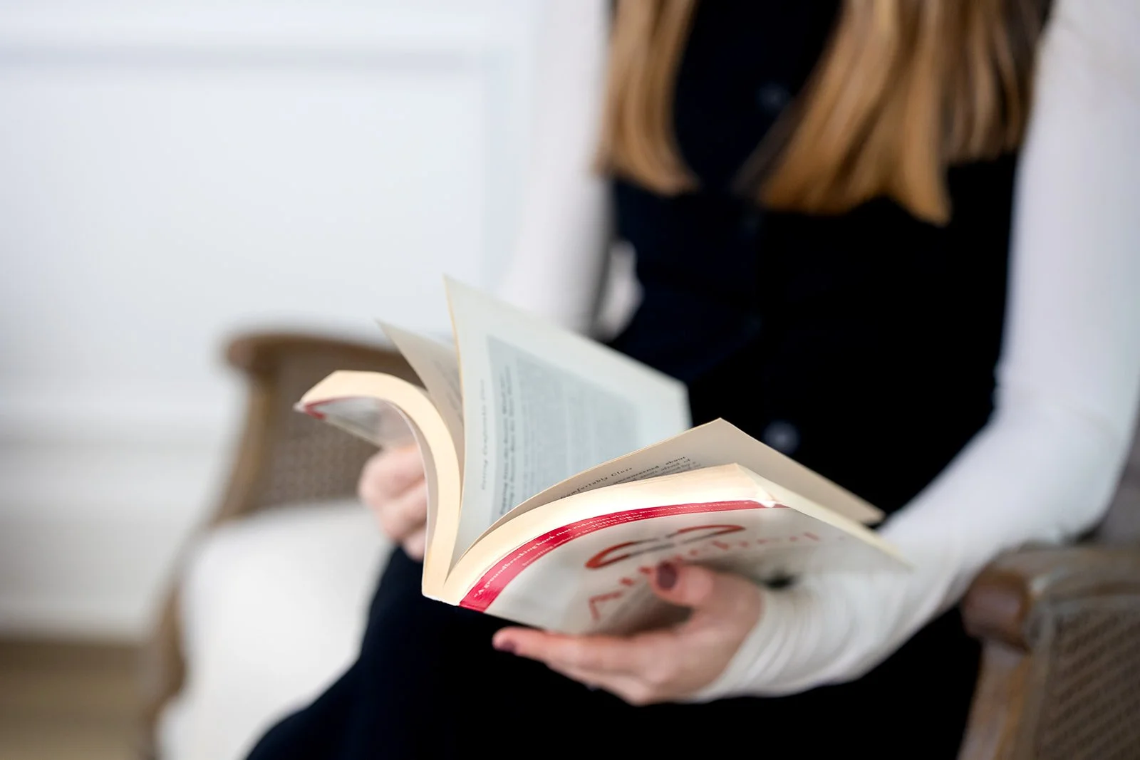 Close up of woman sitting on a chair, holding and reading an open book.