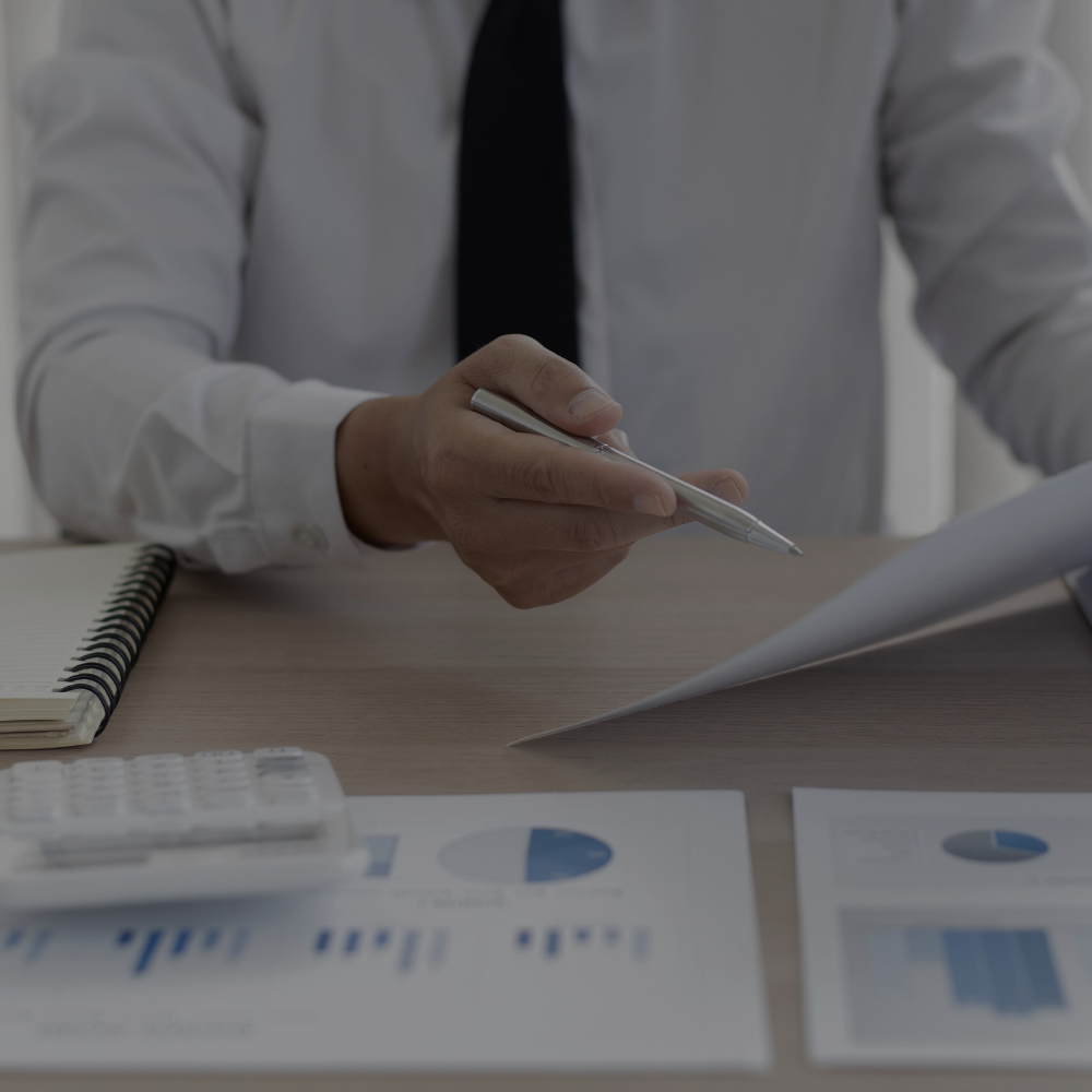 Person in white shirt and black tie reviewing financial documents at a desk with graphs and a calculator.