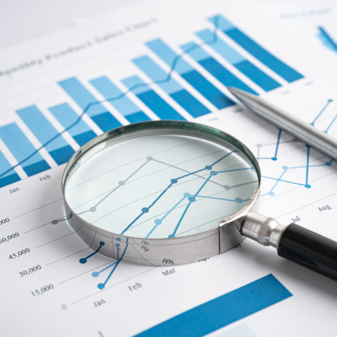 Magnifying glass placed over financial charts showing blue line and bar graphs, focusing on data trend analysis.