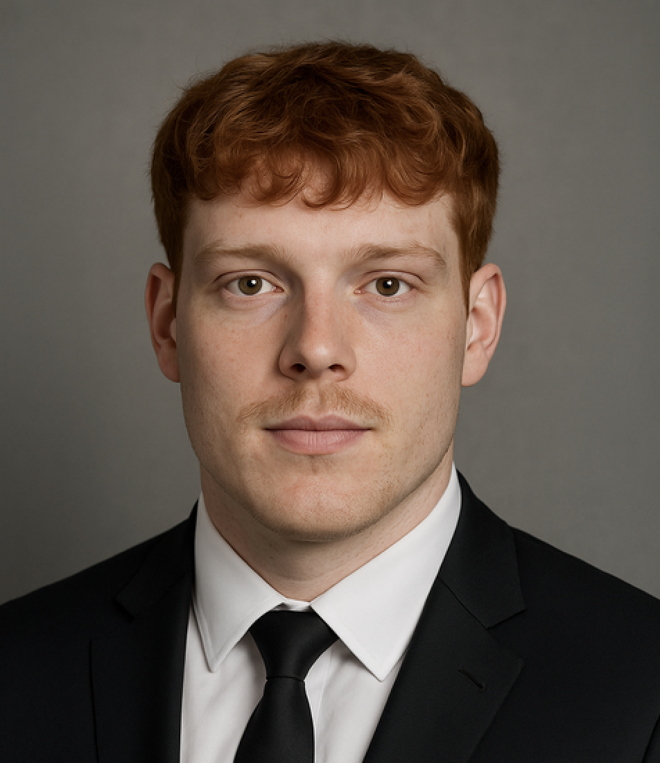 Headshot of a young man with red hair, wearing a black suit, white shirt, and black tie, against a gray background.