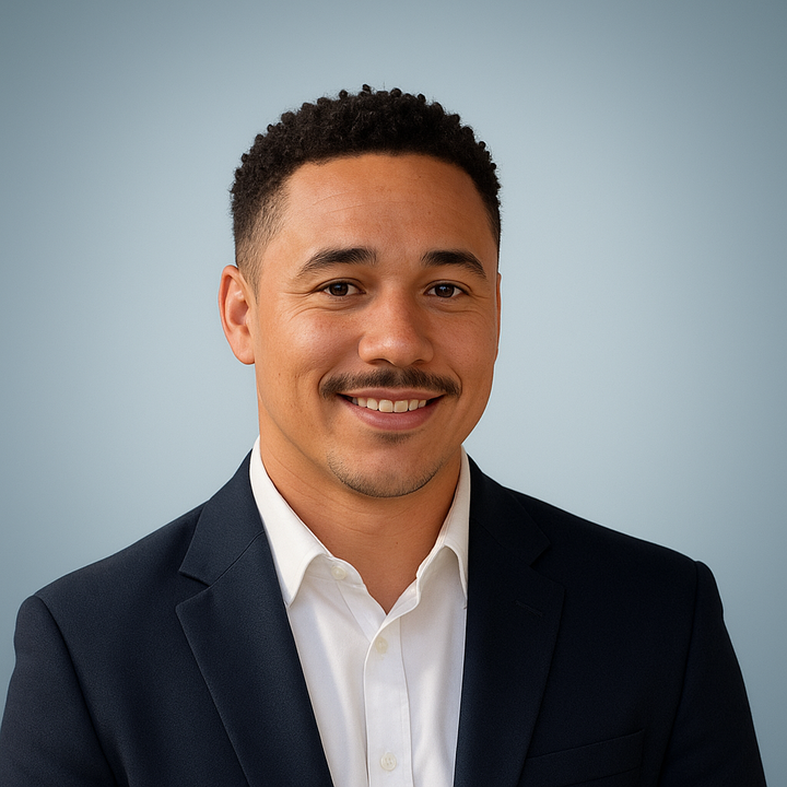 A young man in a suit smiling at the camera against a plain light blue background.