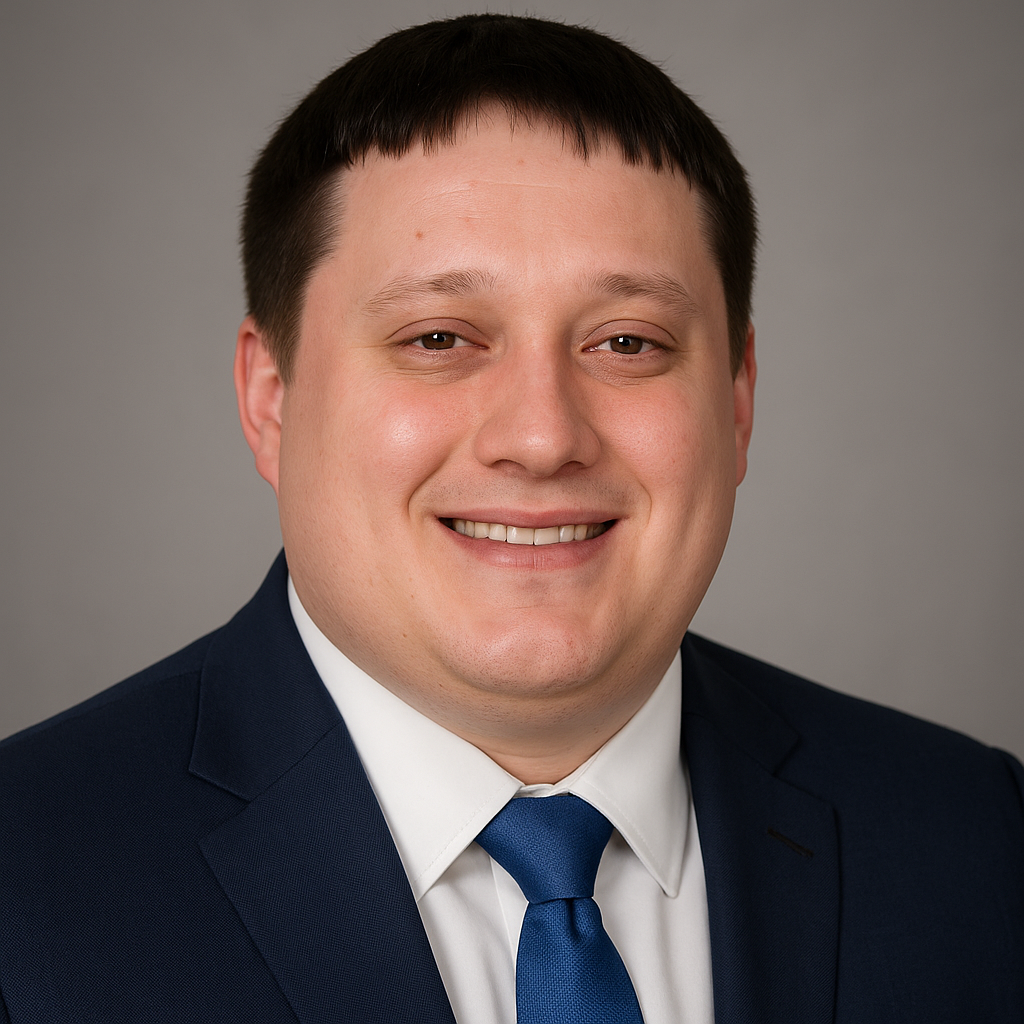 Headshot of a smiling man in a dark suit, white shirt, and blue tie against a gray background.