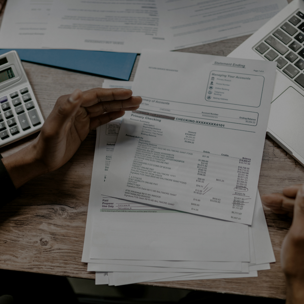 Person reviewing a bank statement at a desk with a calculator and laptop.
