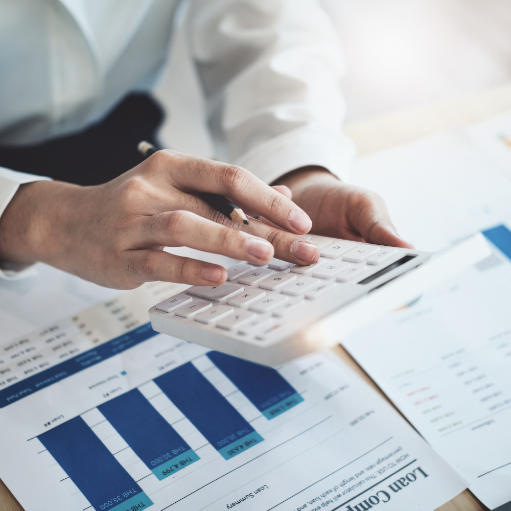 Person using calculator with financial documents and graphs on desk.
