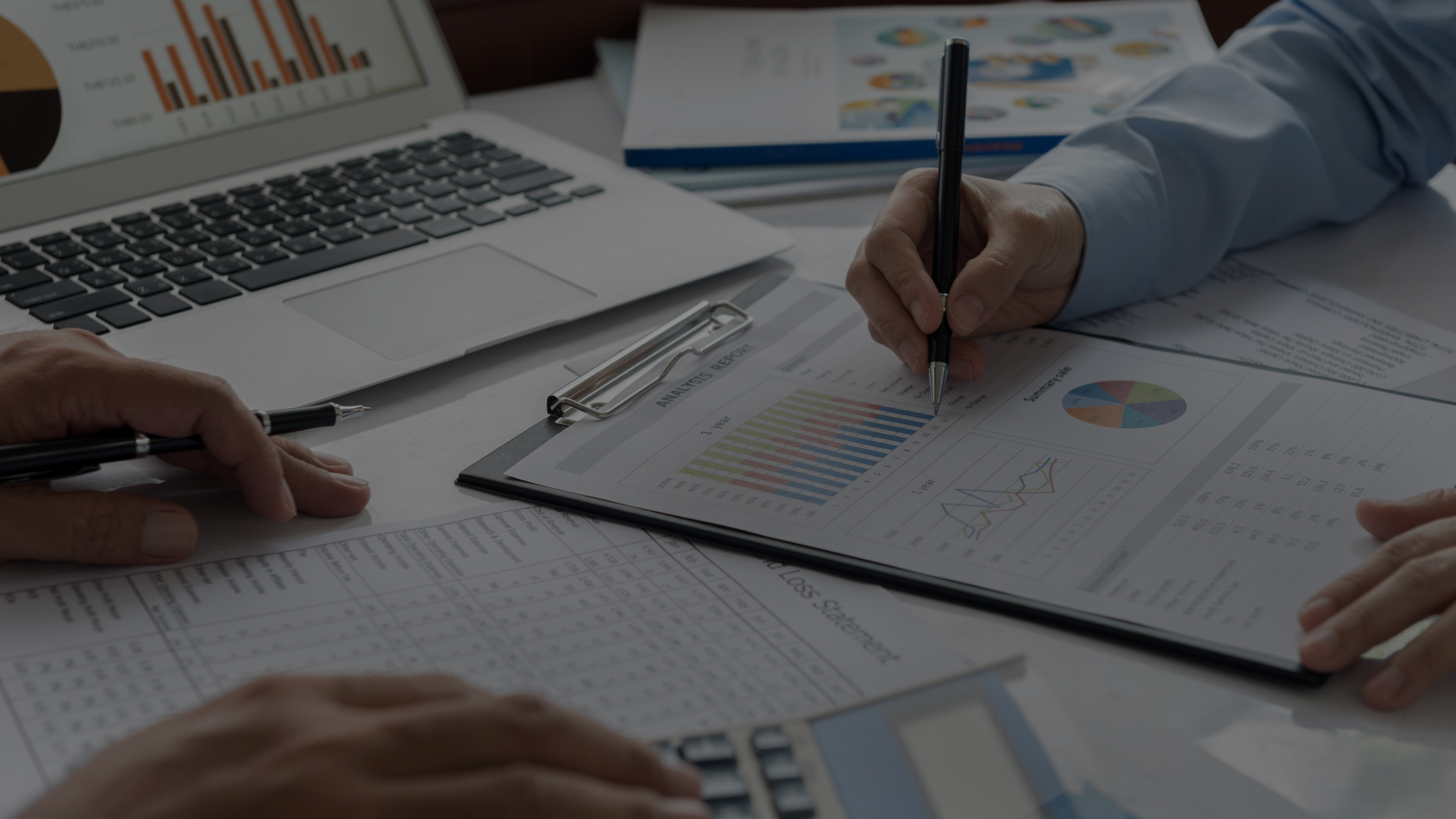 People working on financial reports and analyzing charts and graphs on a desk with a laptop and printed data sheets.