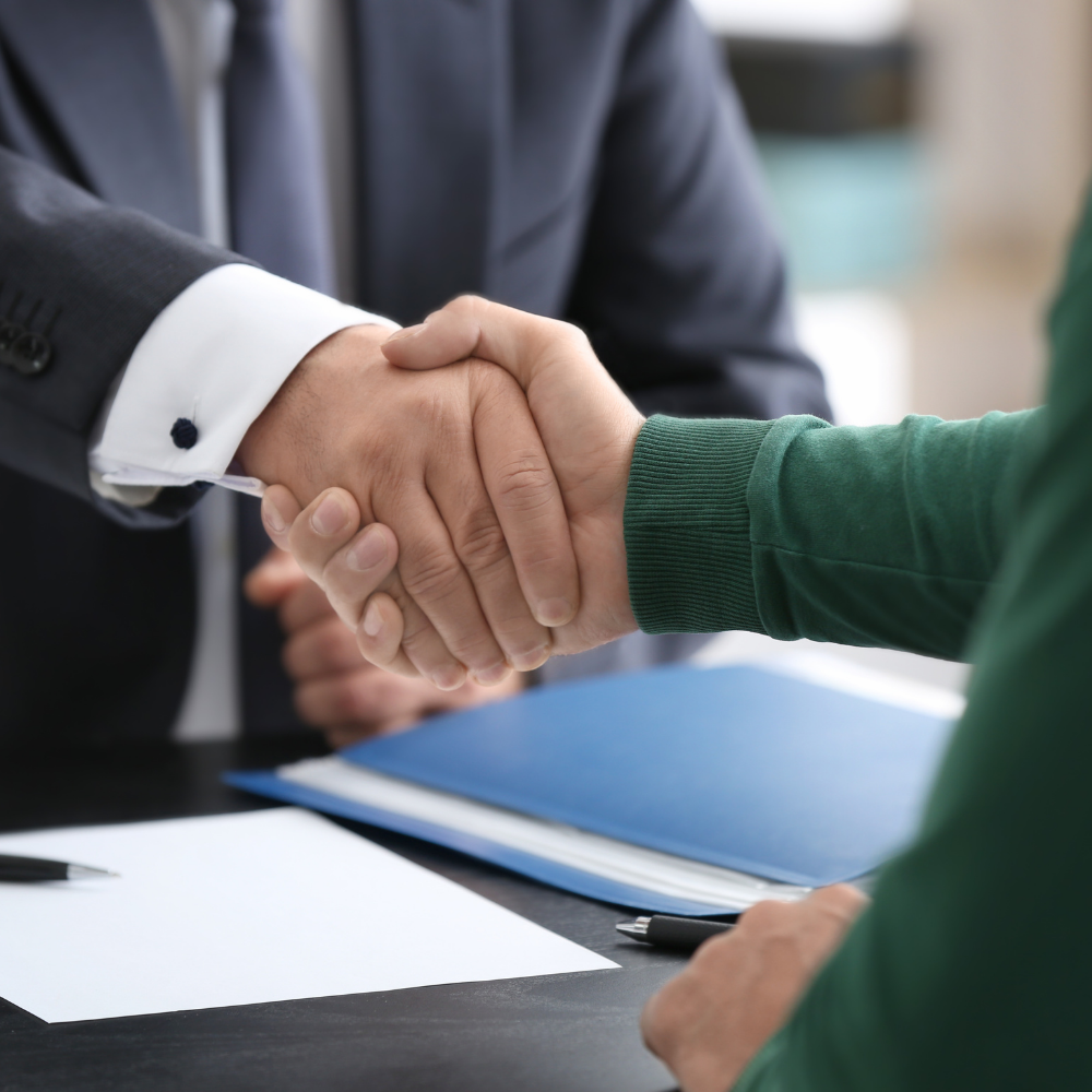 Two people shaking hands over a table during a professional meeting or agreement.