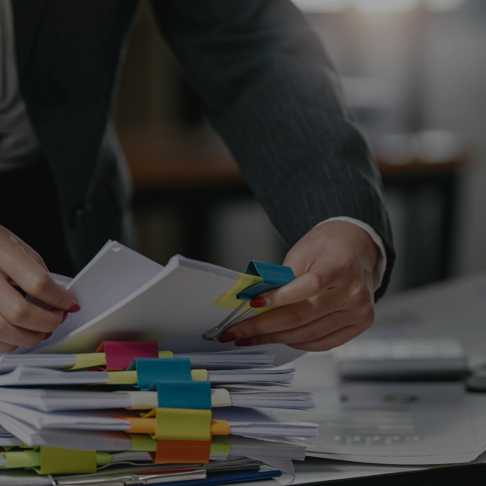 Person in a suit organizing documents with colorful paper clips on a cluttered desk.