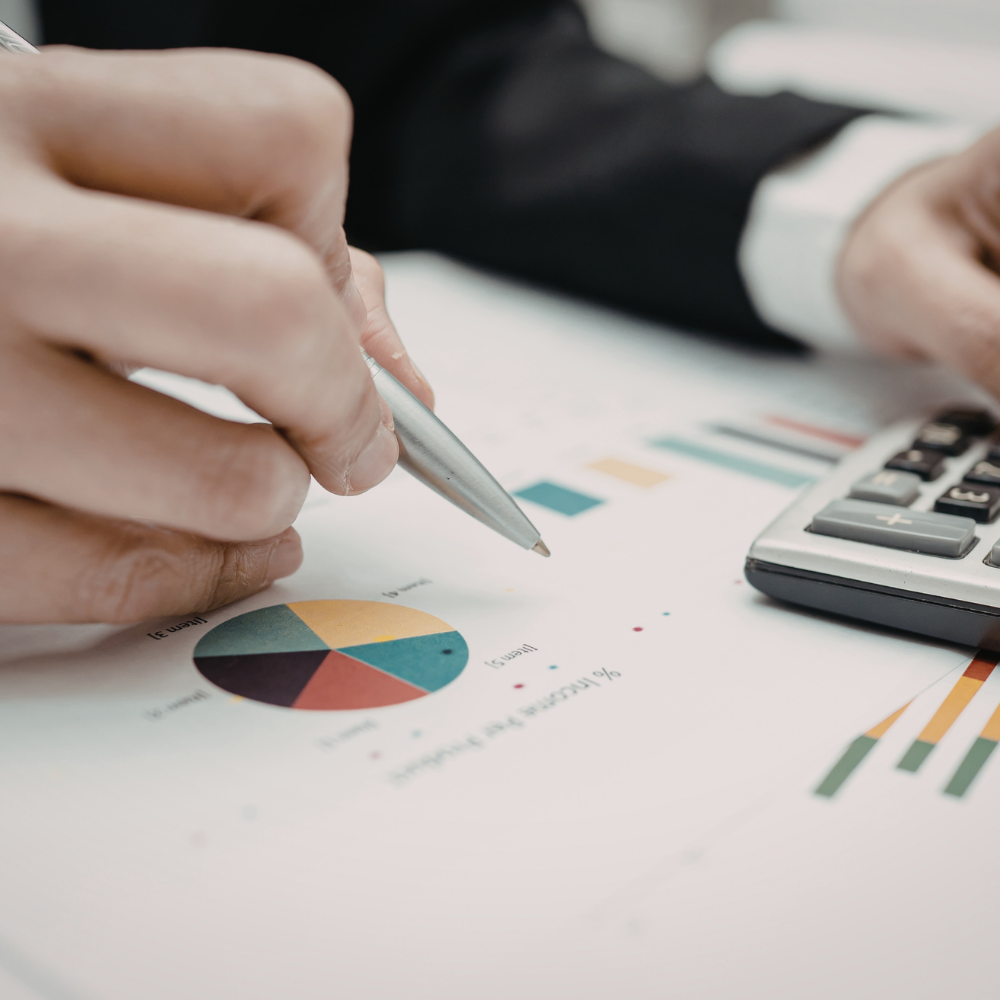 Close-up of a person pointing at a colorful pie chart on a sheet of paper, with a calculator nearby, indicating financial or business analysis.
