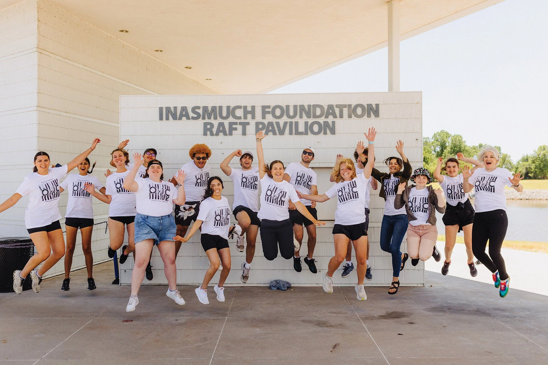 A group of people jumping in the air in front of a sign that reads 'Inasmuch Foundation Raft Pavilion'.