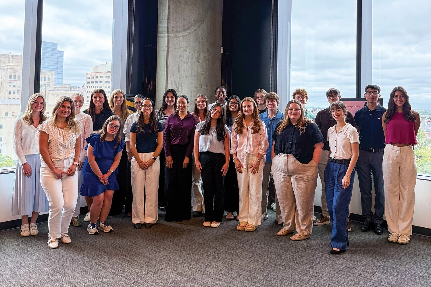 Group of diverse young professionals standing inside a modern office with large windows overlooking a cityscape.